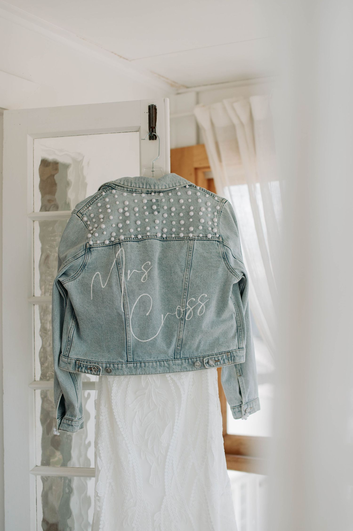 Light blue denim jacket with pearl embellishments and Mrs Cross text hanging on display.