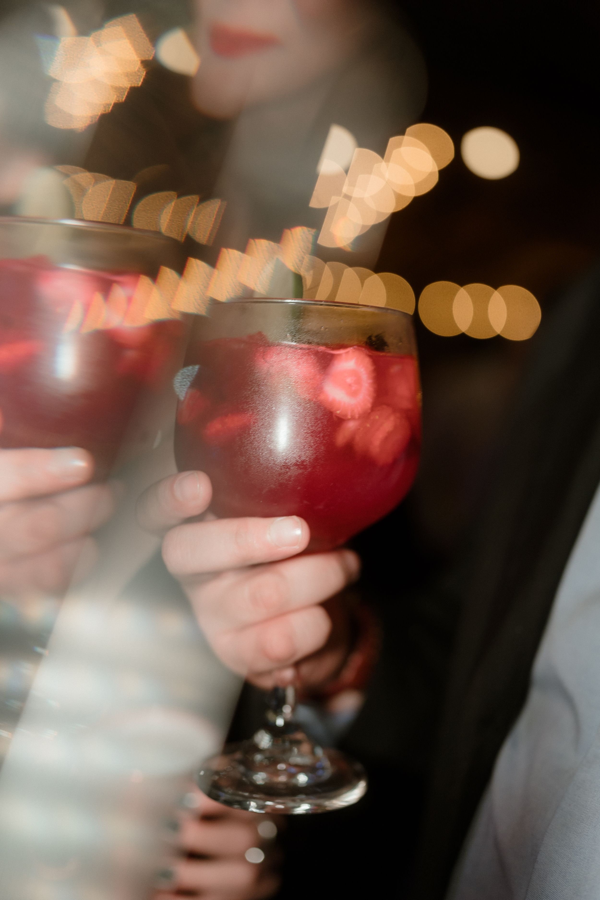 Close-up of red cocktails in wine glasses with bokeh lights in background.