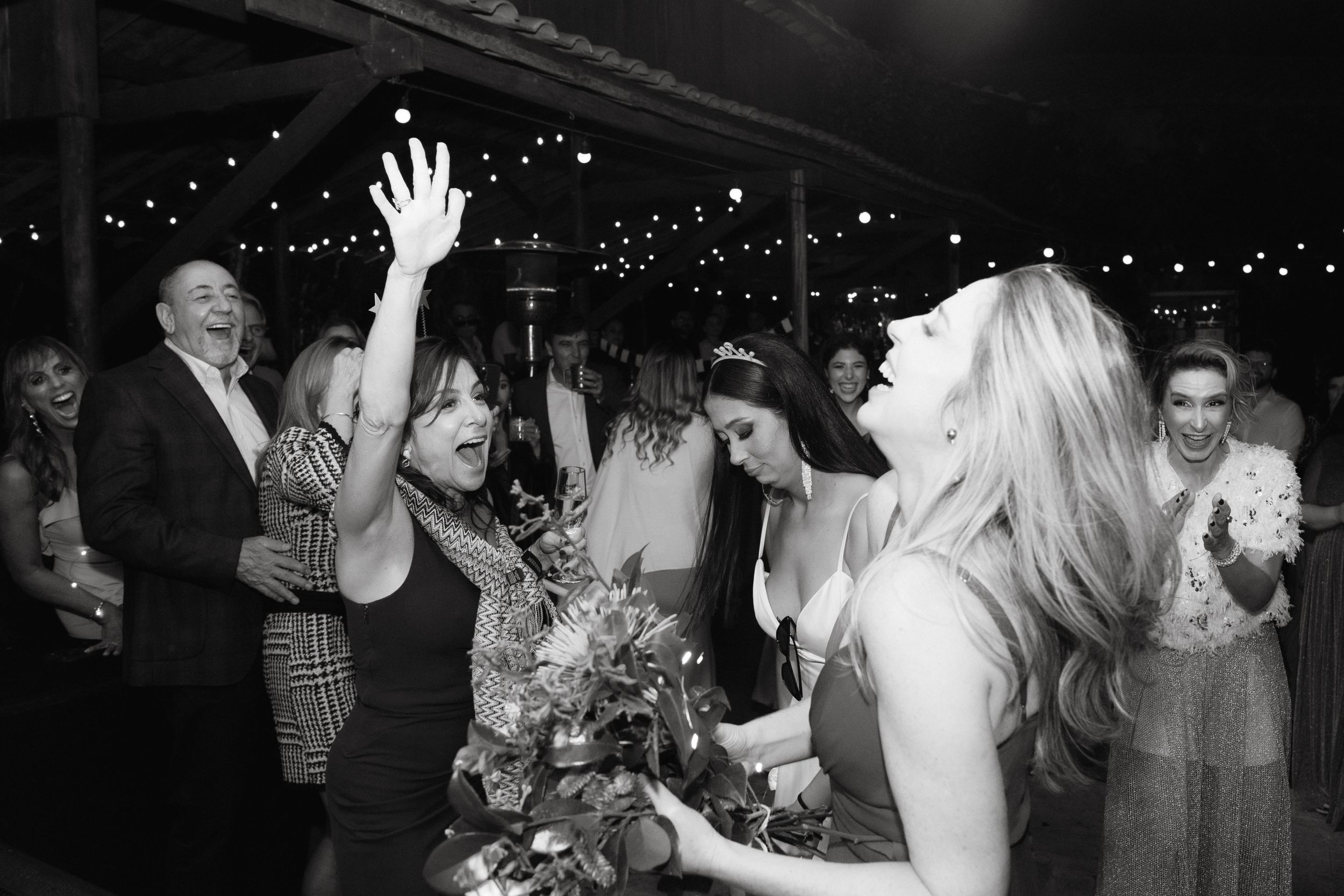 Wedding reception guests dancing and celebrating with raised arms under string lights.