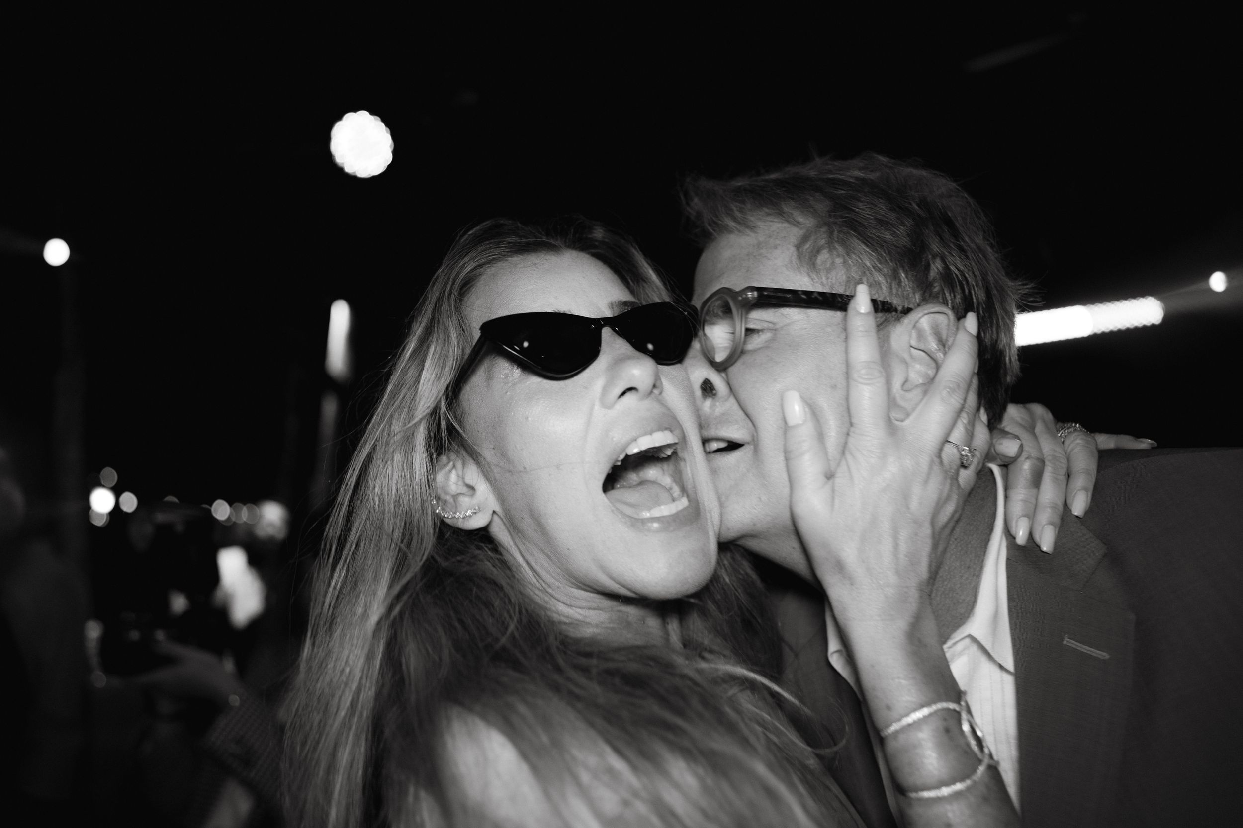 Party guests laughing and celebrating under night lights wearing sunglasses.