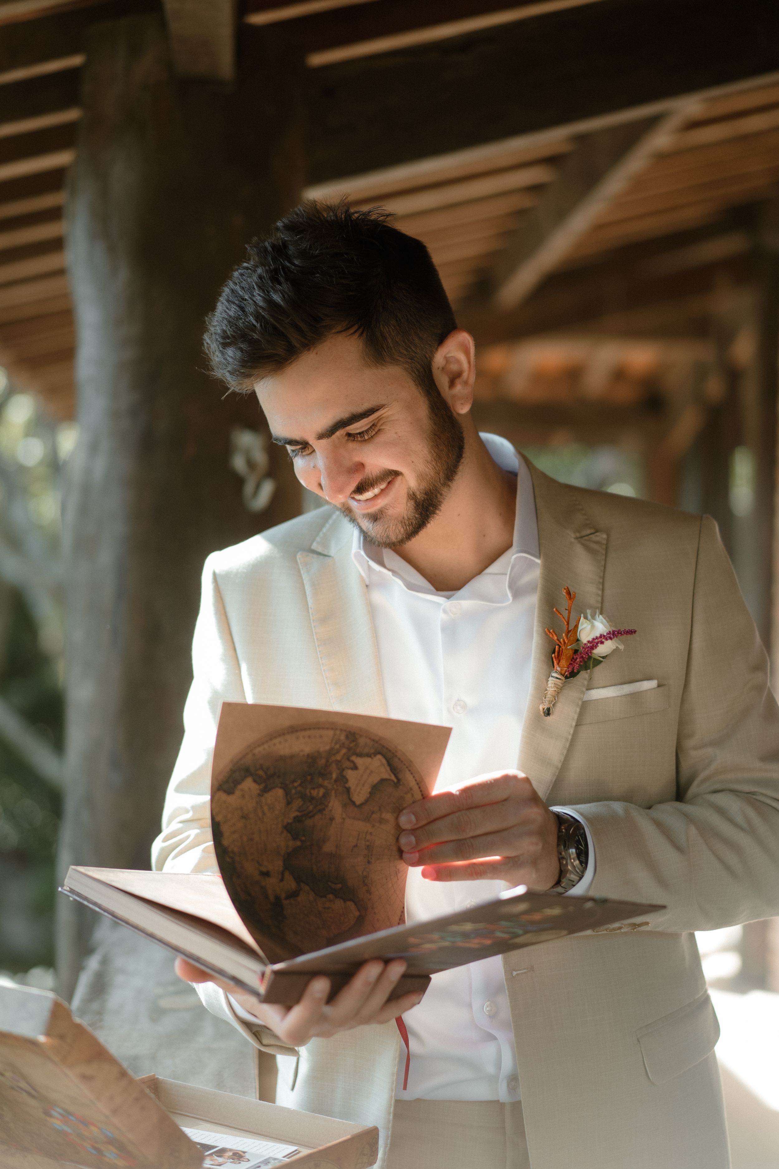 Person in beige suit jacket smiling while reading a book with a boutonniere on lapel.