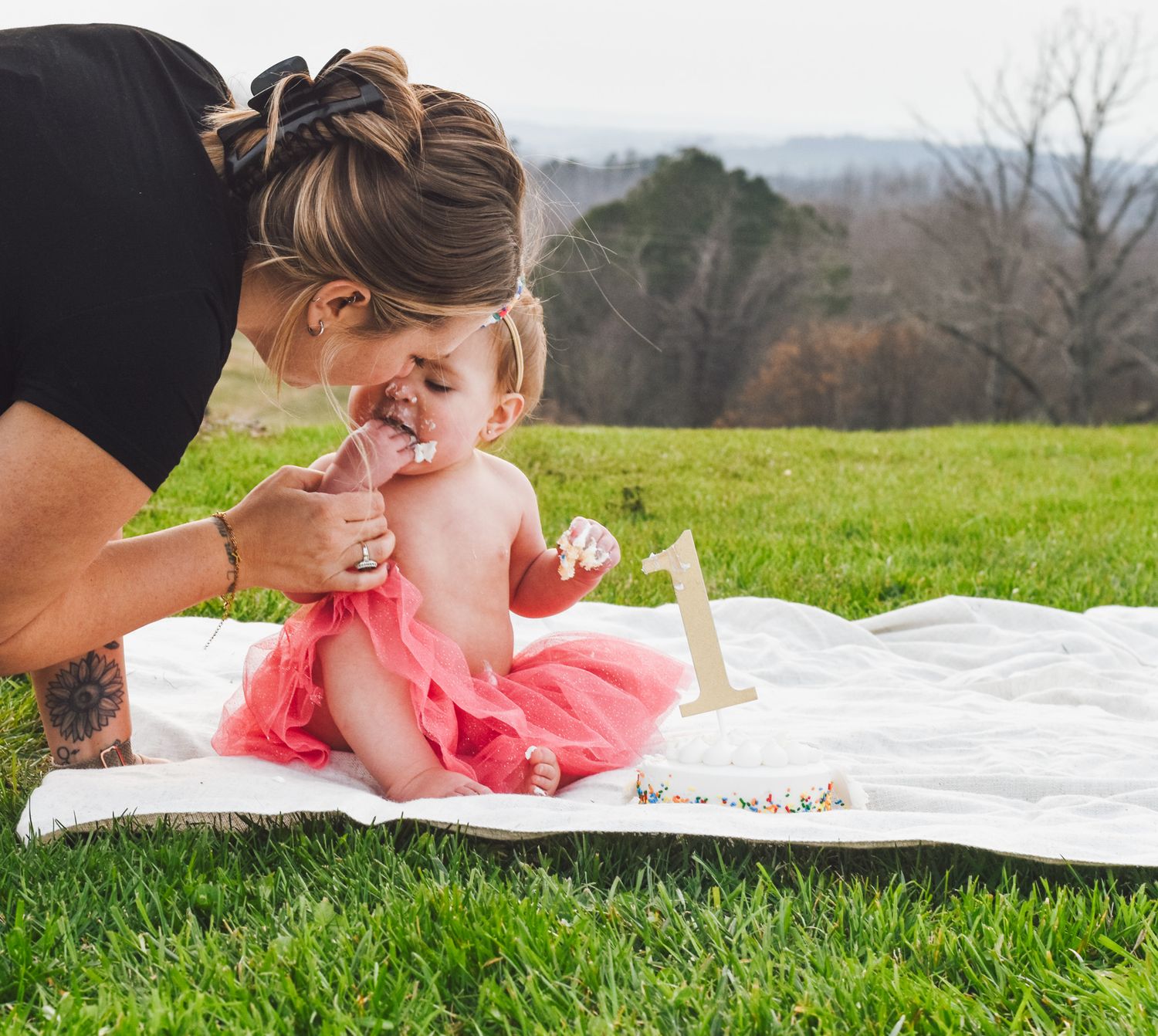 Sweet celebration moment captured outdoors on white blanket with pink tulle dress.