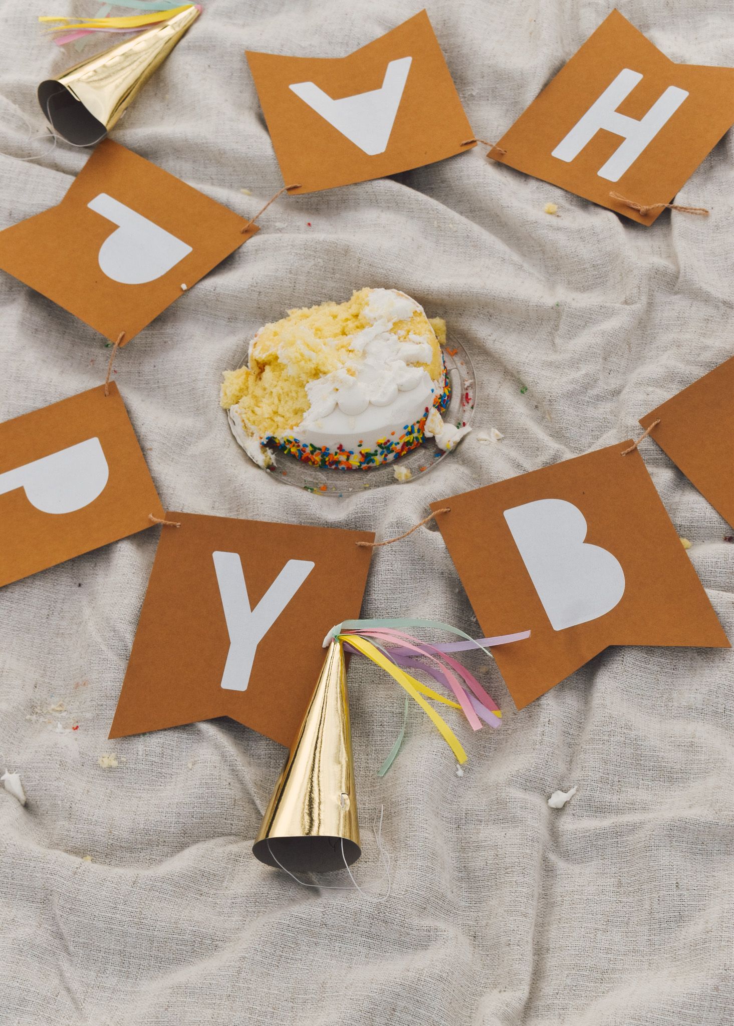 Party decorations and snacks scattered on a gray linen surface with brown letter cutouts.