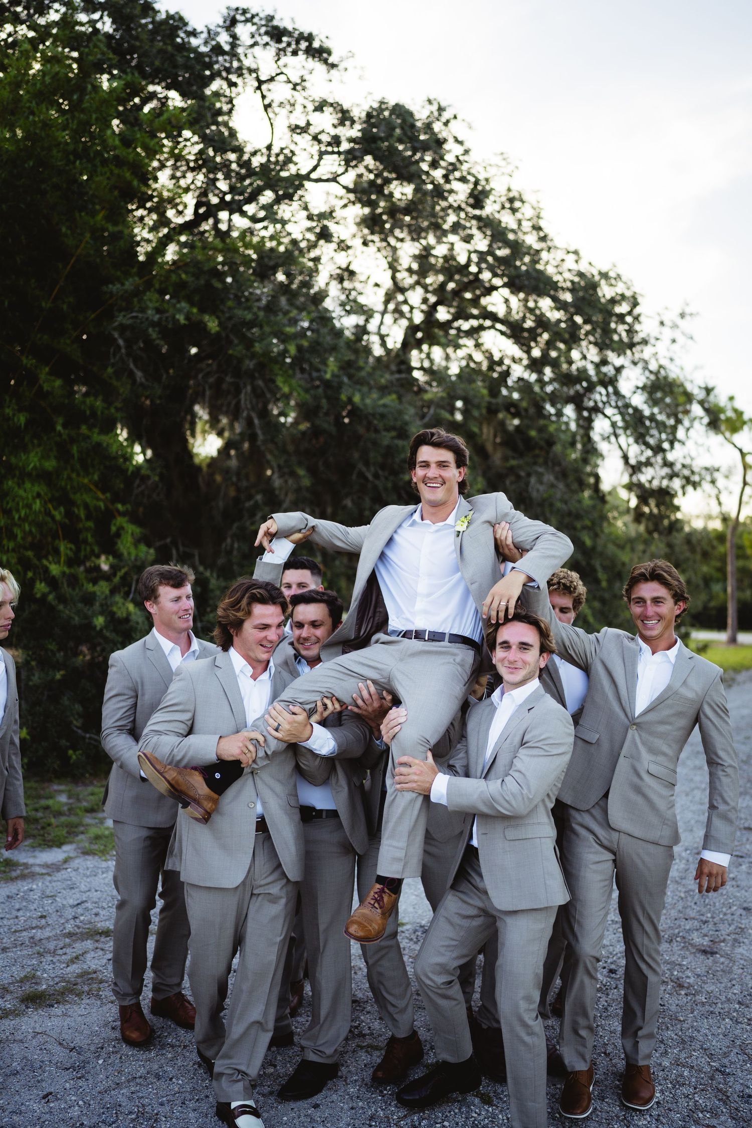 A lively group in matching gray suits posing playfully together in an outdoor setting at sunset.