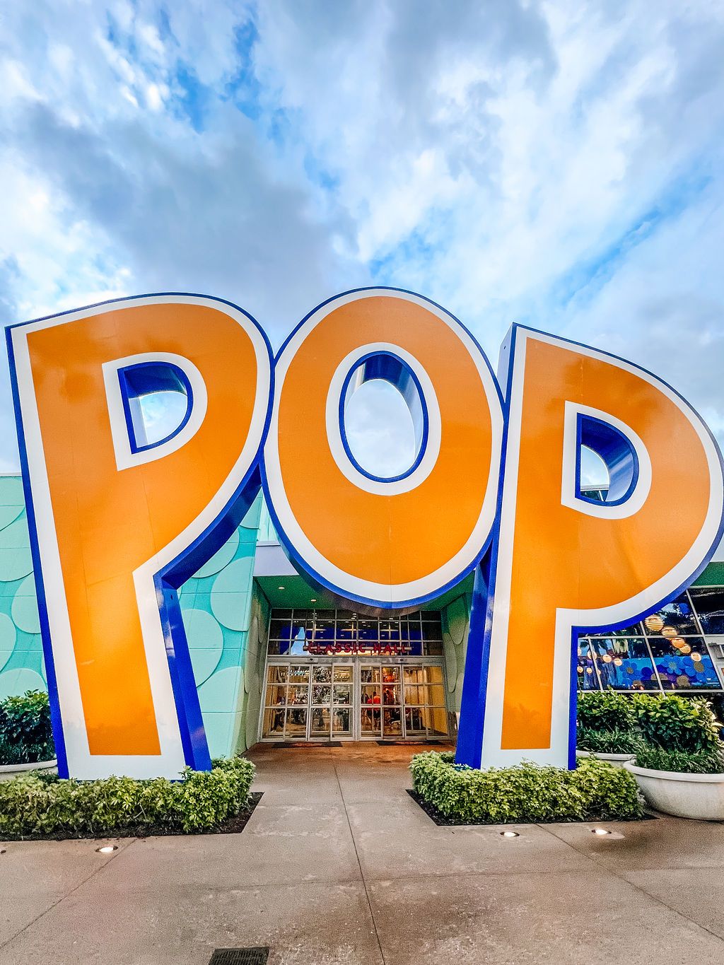 Large orange and blue text spells POP in a creative wall mural installation against a bright blue sky.