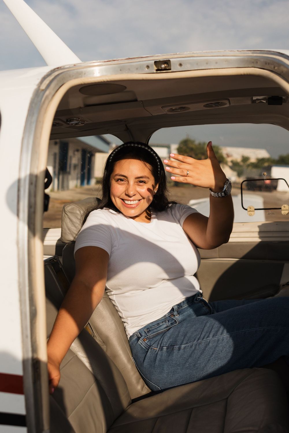 A passenger relaxes in a small aircraft's cabin wearing a white t-shirt and jeans on a sunny day.