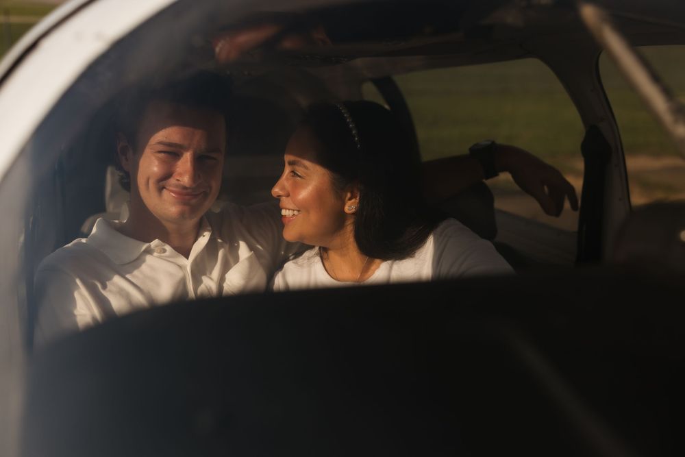 Through a car window, two people in white shirts share a joyful moment while seated together.