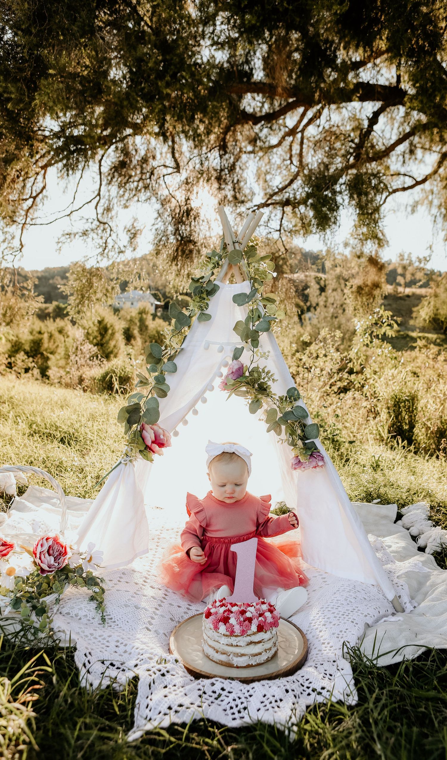 Girl sitting in a teepee for an outdoor cake smash