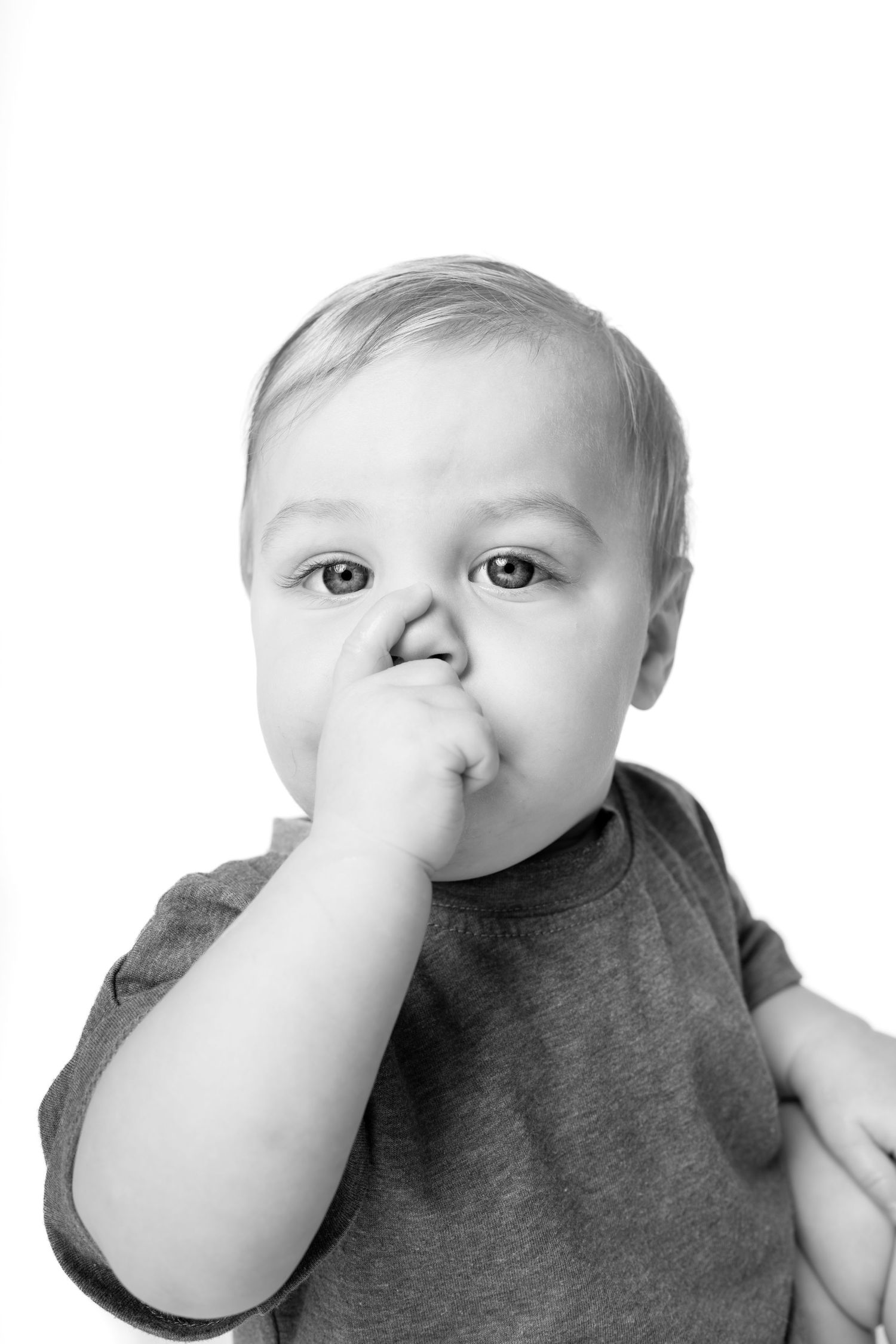 Black and white portrait of a cute baby boy with hand near mouth, looking at camera on white background.