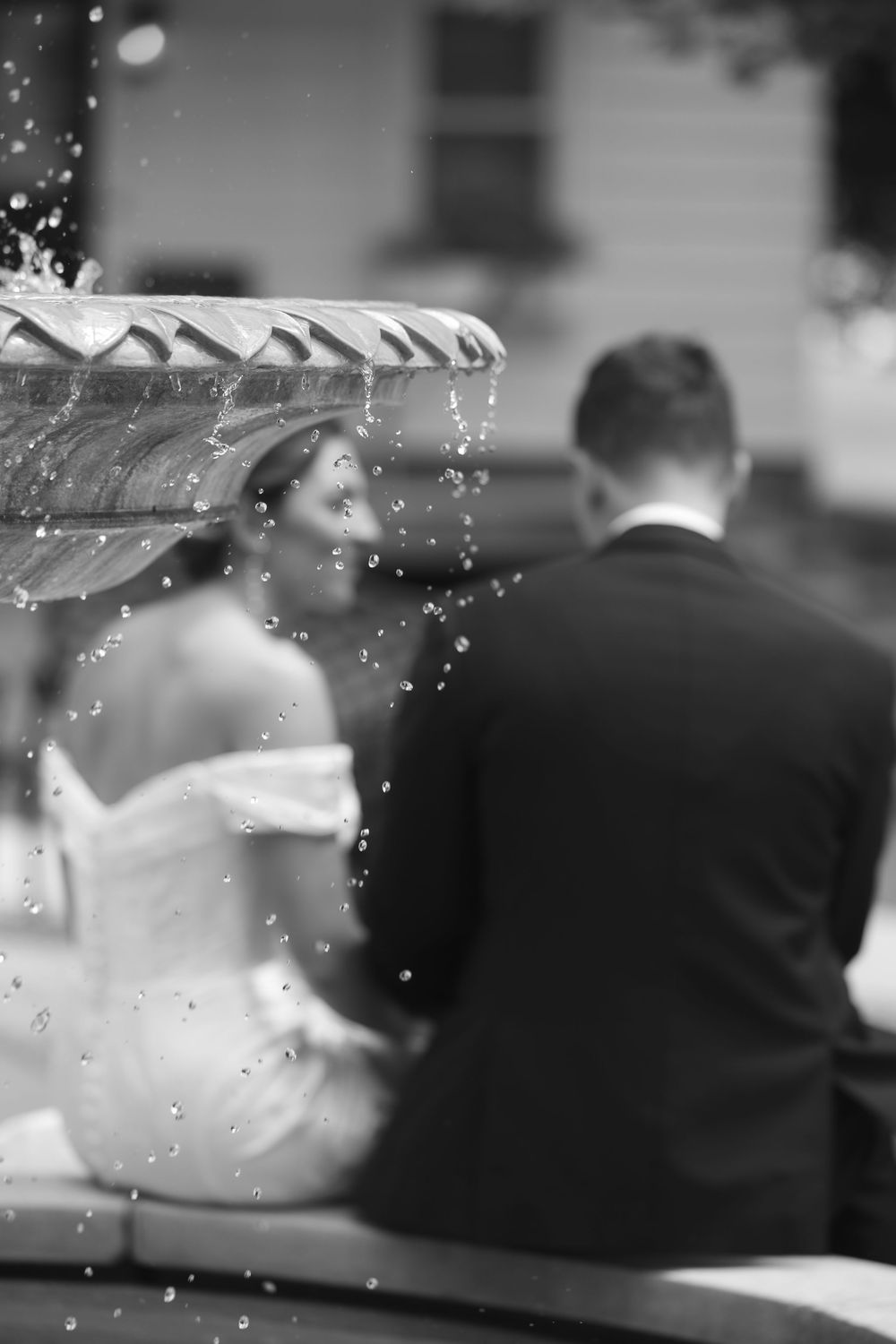 A black and white wedding photo shows water droplets falling from an umbrella while a couple sits beneath it.