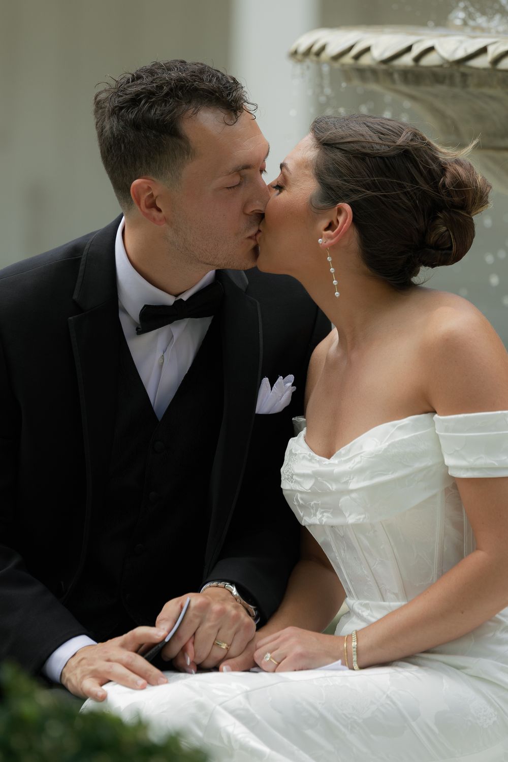 A romantic wedding moment captured of a bride in white gown and groom in tuxedo sharing a tender kiss.