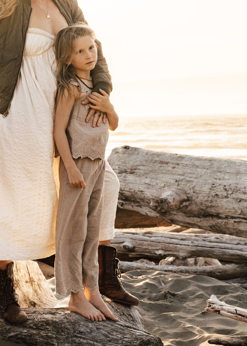 A toddler walks along the beach at sunset with an adult, showing sandy footprints along the shoreline.