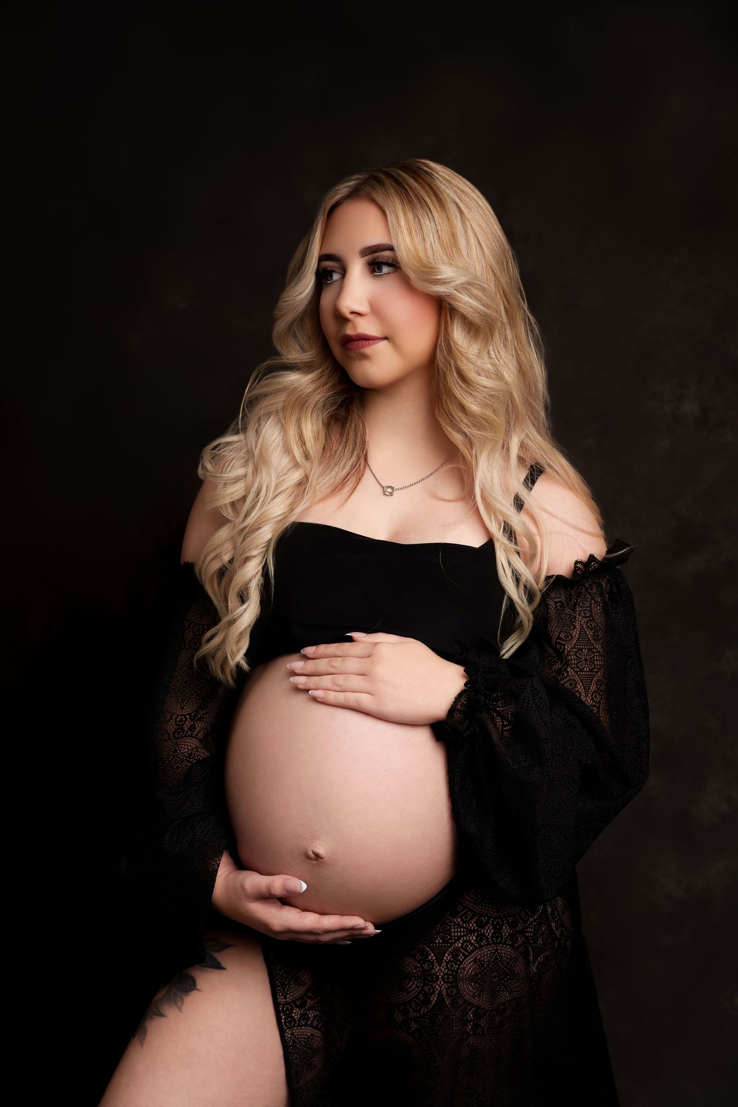 Glamorous maternity photo with black lace robe against moody dark background.