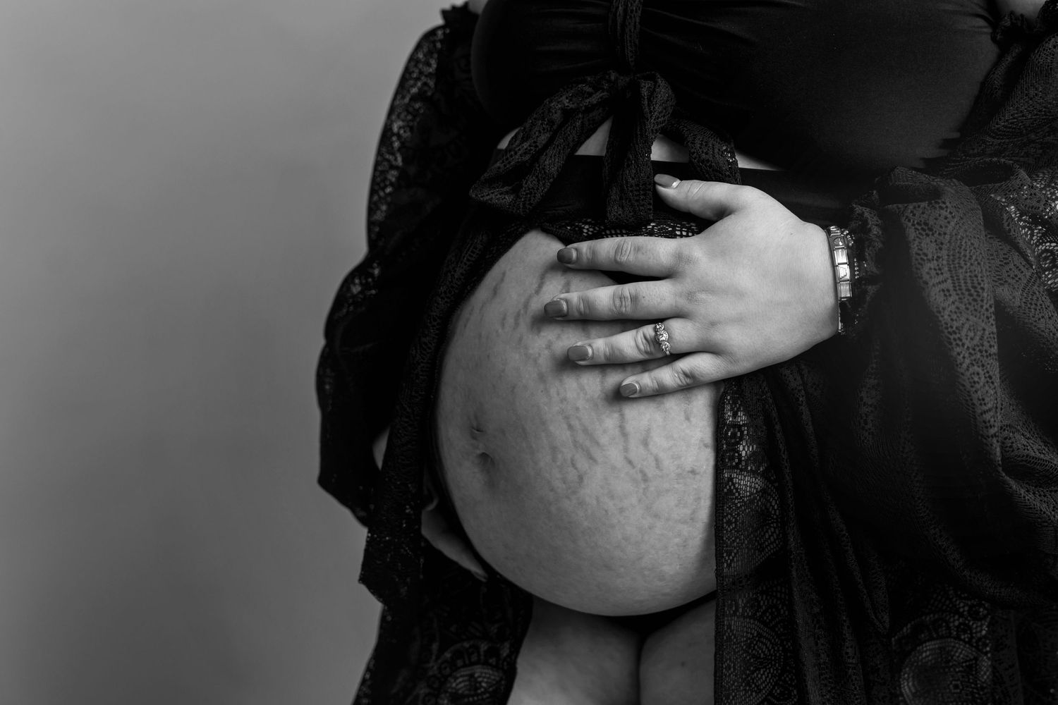 Black and white close-up of pregnant belly with hands gently cradling.