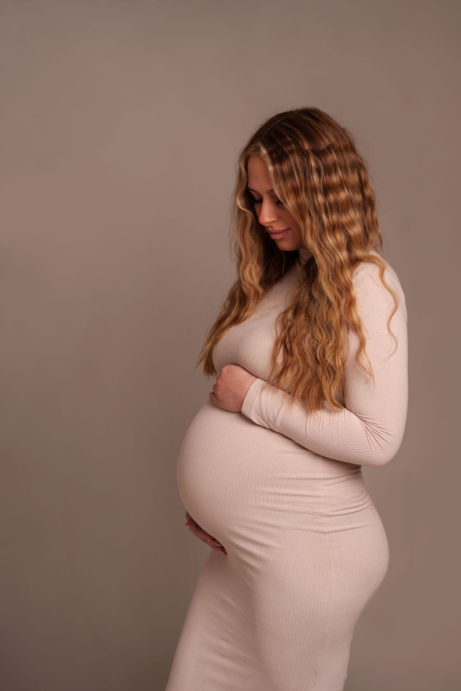 Soft maternity portrait in fitted beige dress showing side profile.
