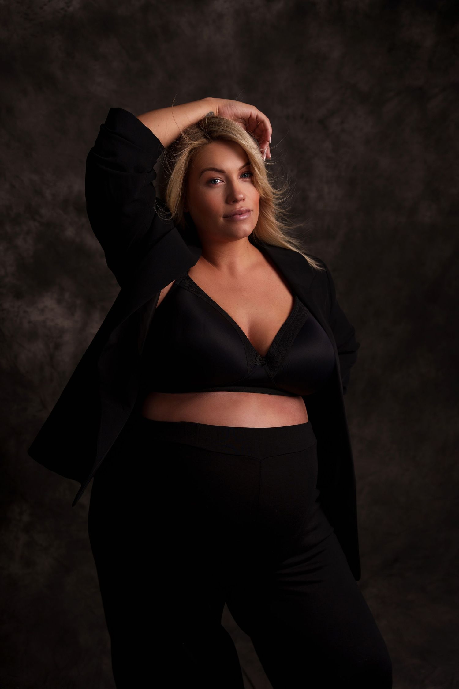 Elegant maternity portrait in all-black outfit with flowing hair against moody backdrop.