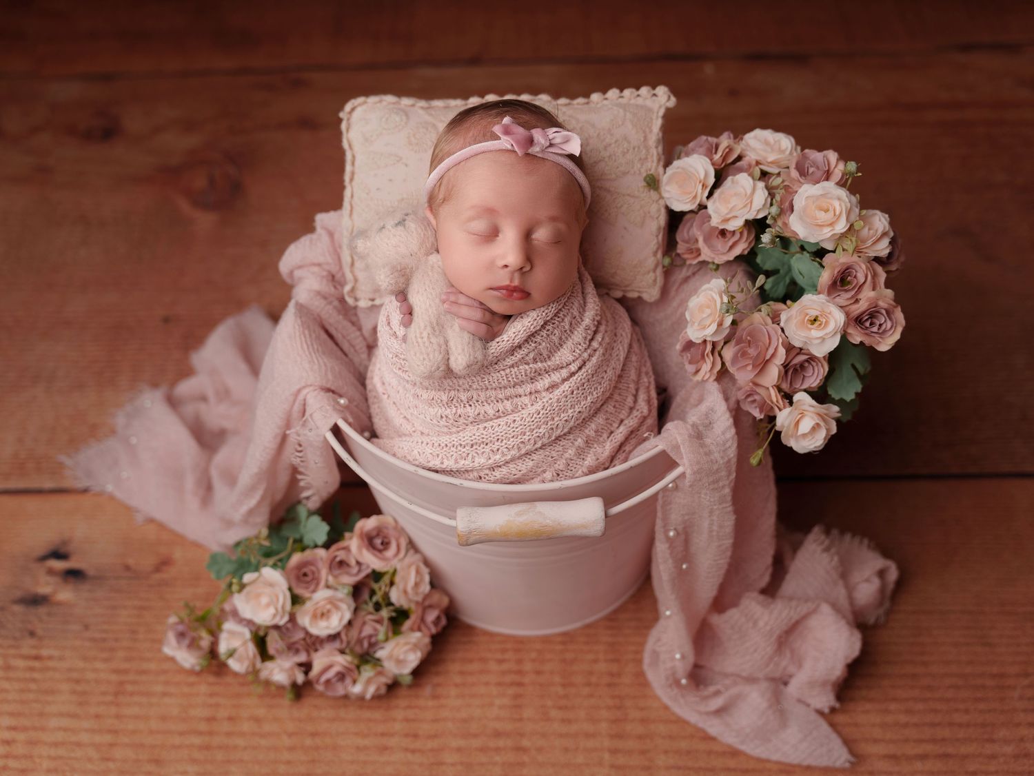 Sleeping newborn in pink cloth surrounded by pink floral arrangements for professional photography session.