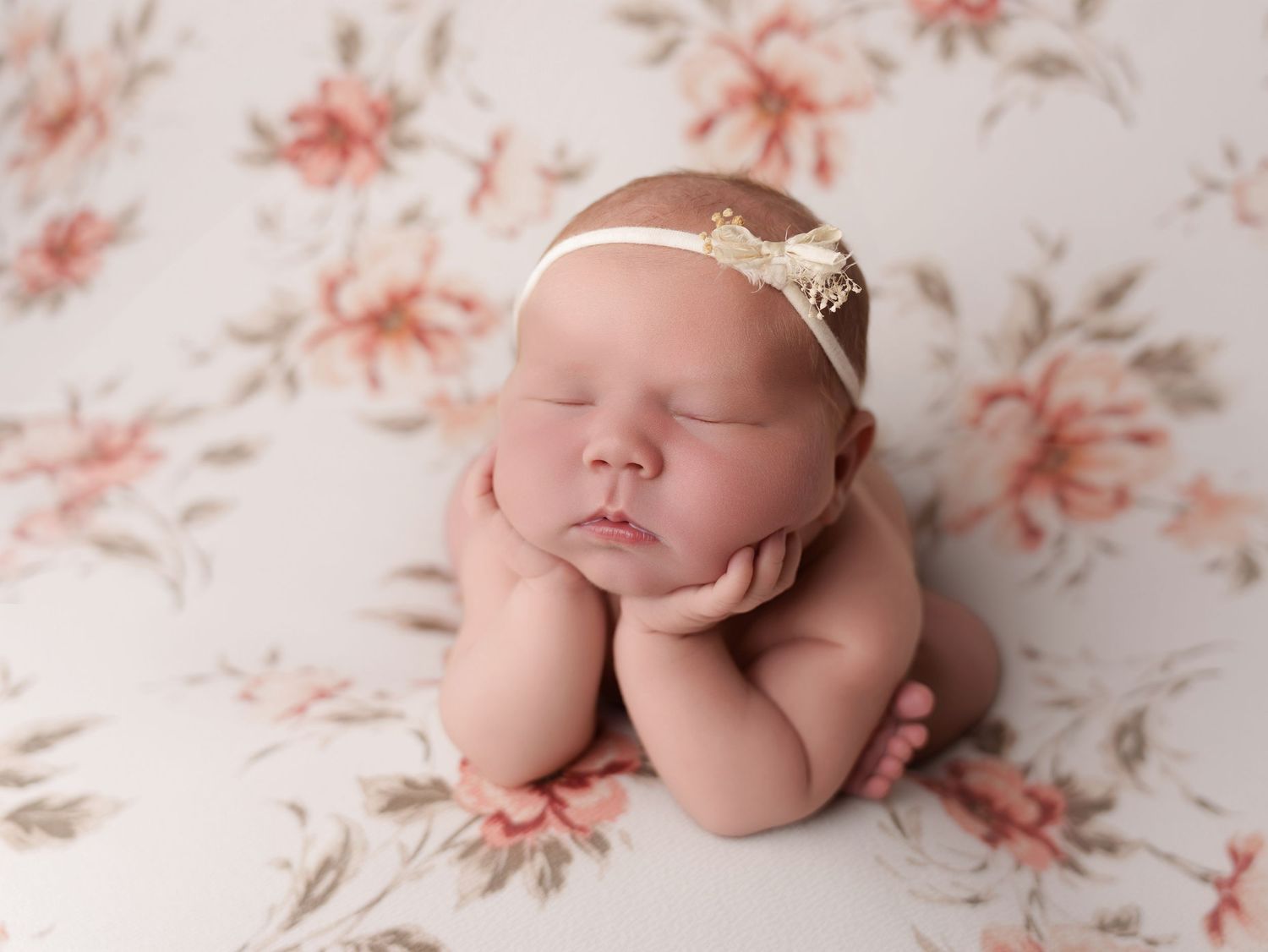 Sleeping newborn in delicate headband poses on floral backdrop during professional photography session.