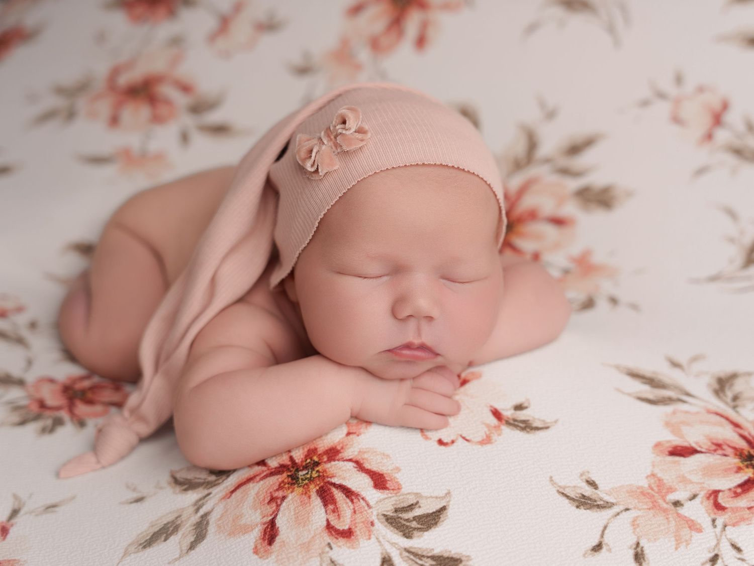 Peaceful sleeping newborn wrapped in soft pink cloth resting on floral pattern background.