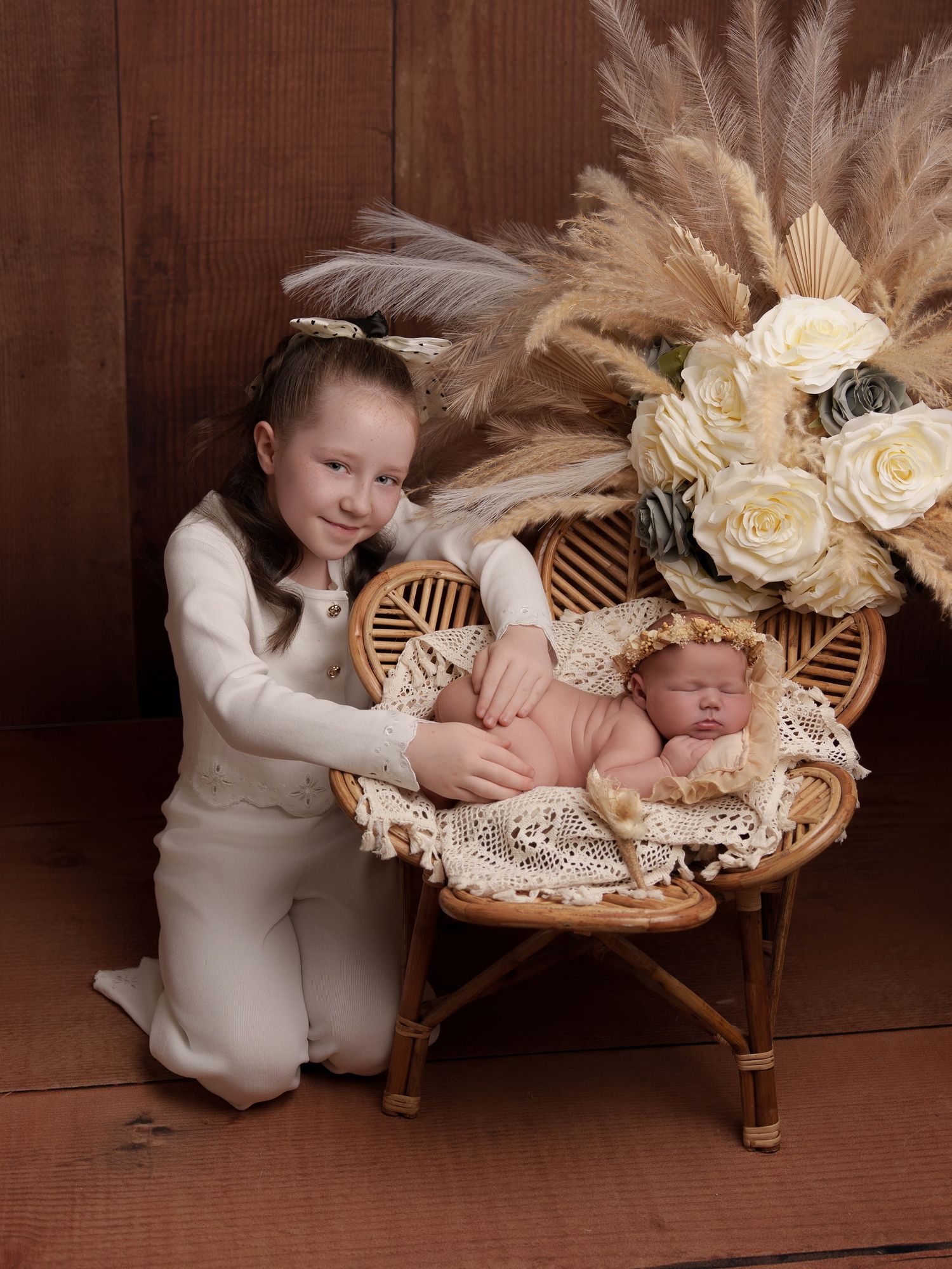 Portrait of two children with bohemian floral decor featuring roses and pampas grass against a brown wooden backdrop.