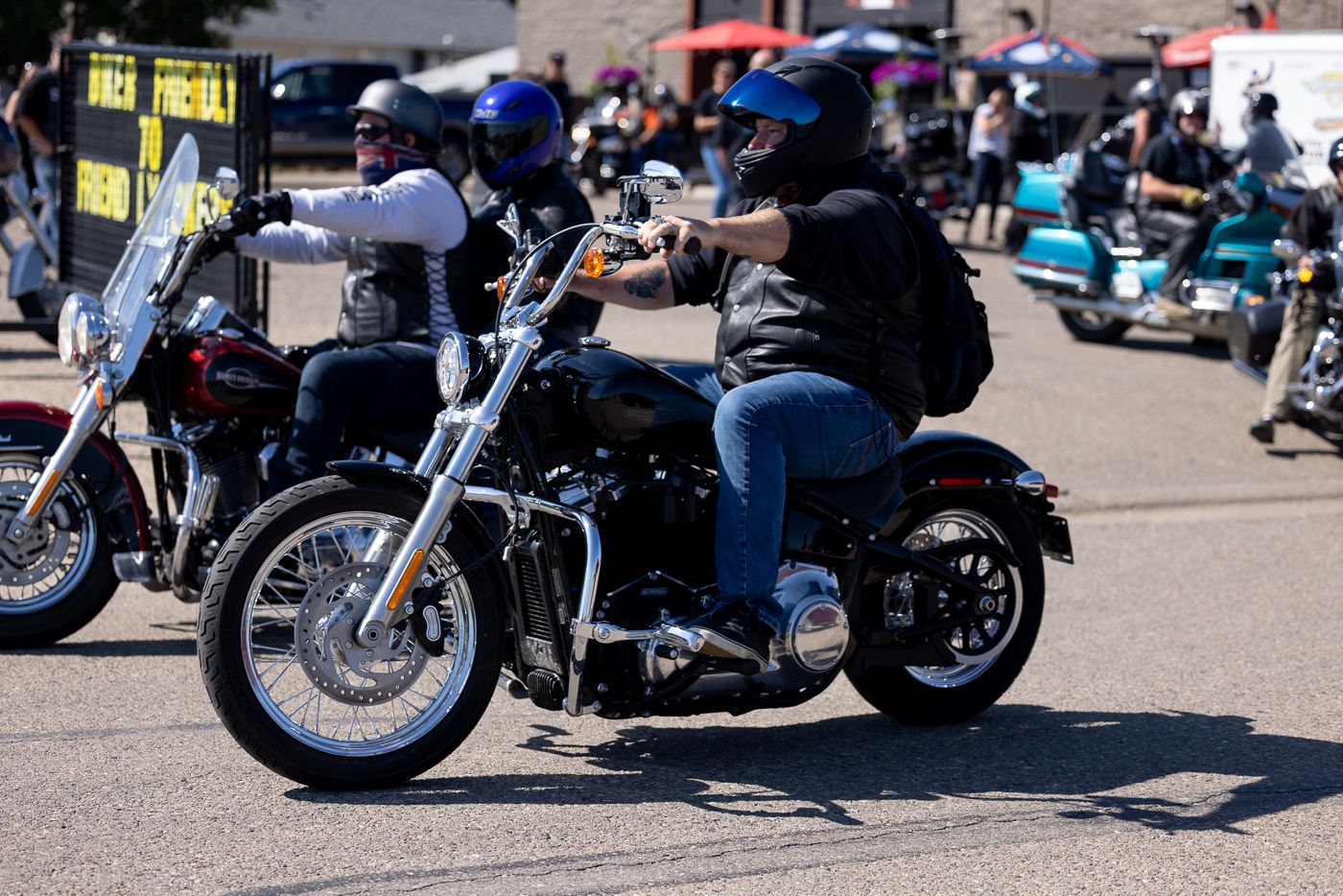 Closeup view of motorcycle wheels and tires parked in a line at an outdoor event on a sunny day.