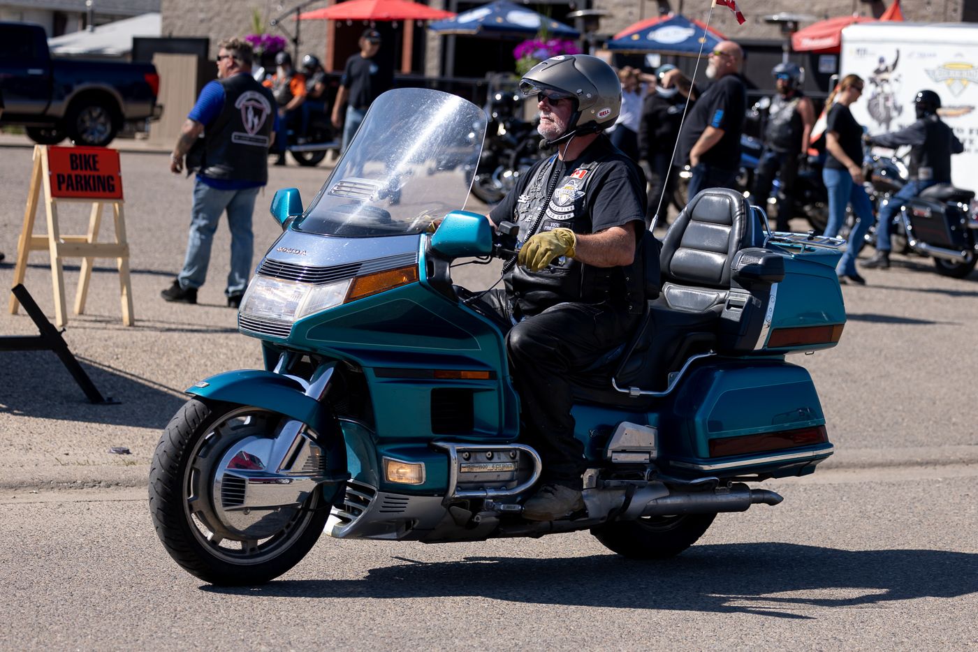 A panoramic view of parked motorcycles and touring bikes at an outdoor event with red tent canopies visible in background.