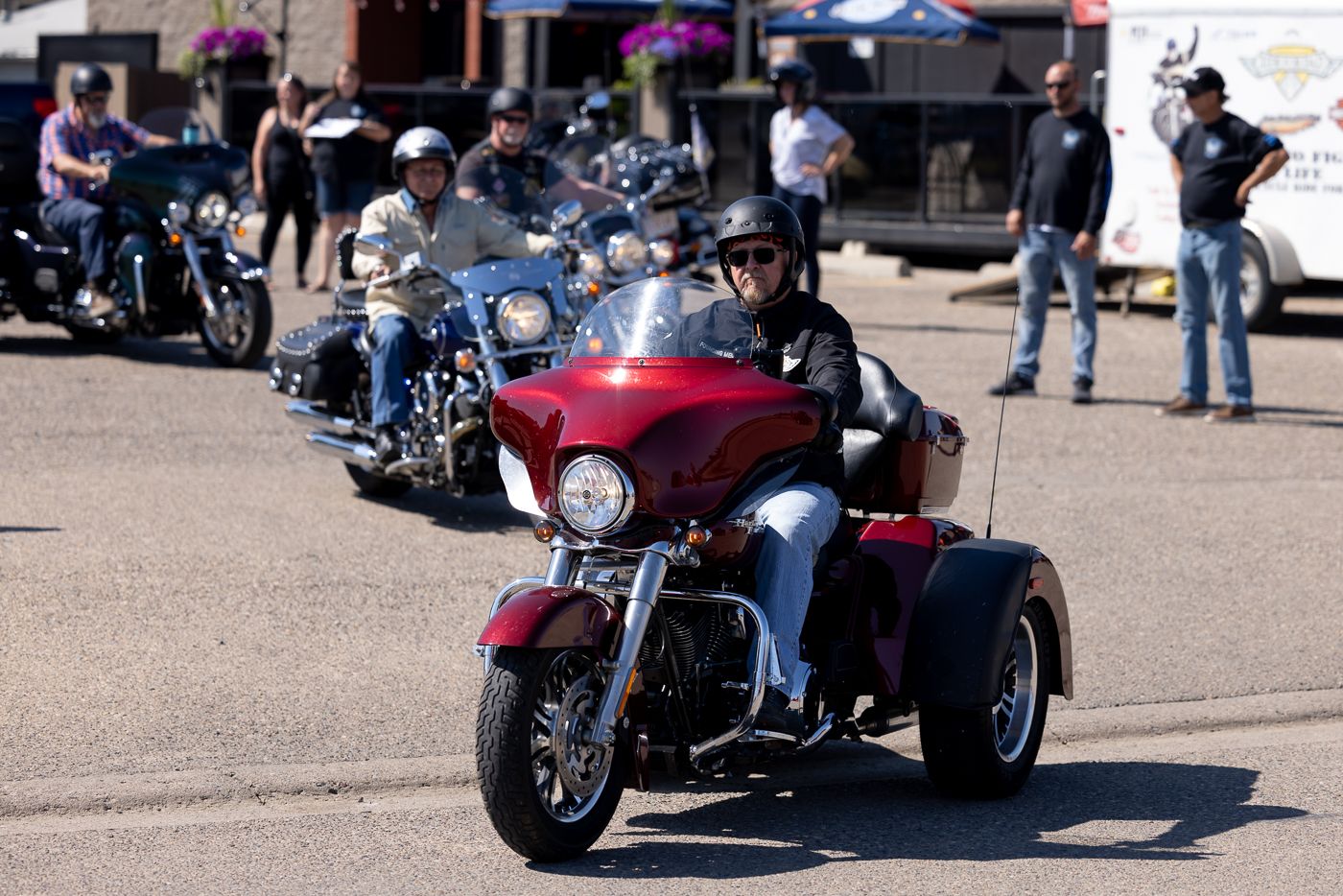 A red three-wheeled motorcycle sits at the front of a line of bikes during a motorcycle gathering.