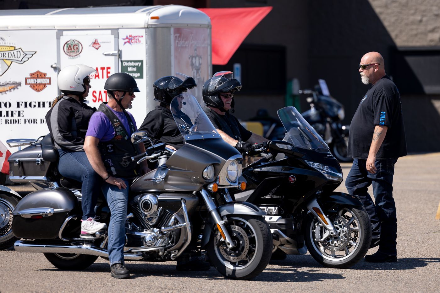 Motorcycle enthusiasts gather around parked motorcycles outside a building on a sunny day.