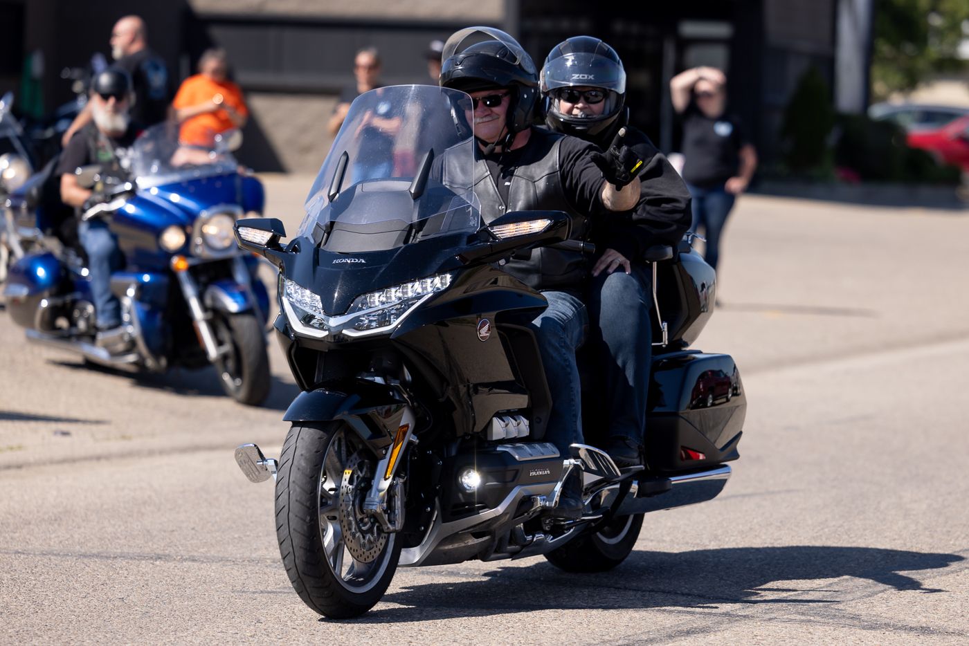 Two motorcycle riders cruise on a black touring bike during a group ride on a sunny day.