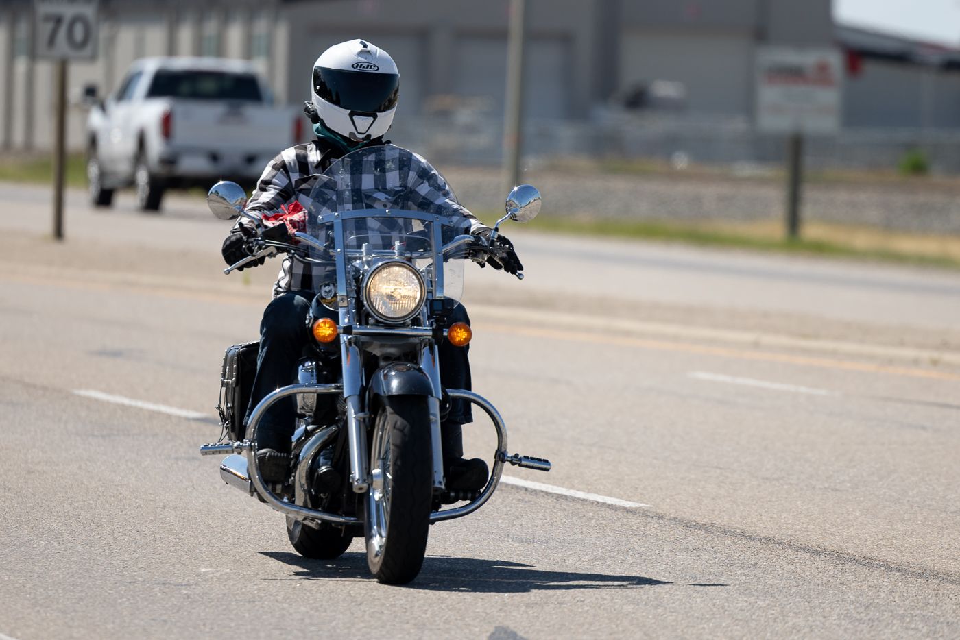 Person riding a black cruiser motorcycle on a road wearing protective gear and helmet.