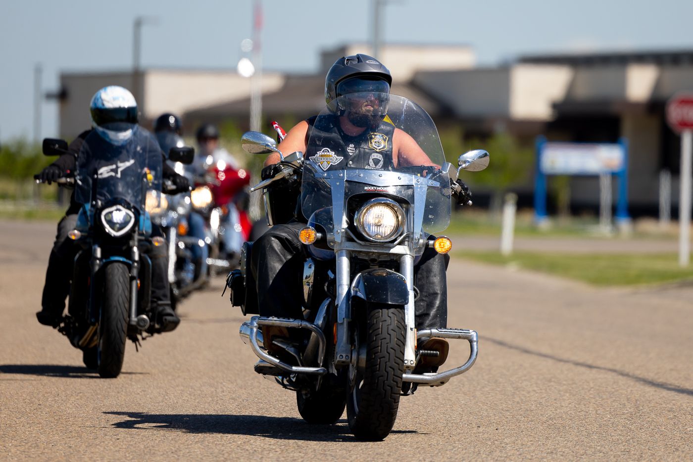 Two motorcyclists riding cruiser-style bikes down a paved road on a bright day.