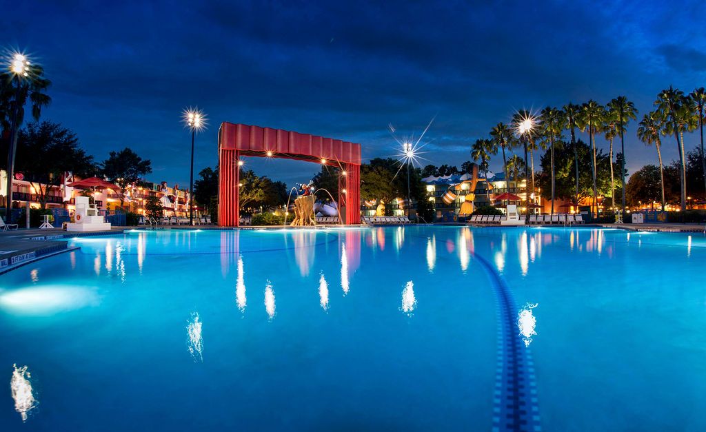 Illuminated swimming pool at Disney's All-Star Movies Resort at night with red archway.