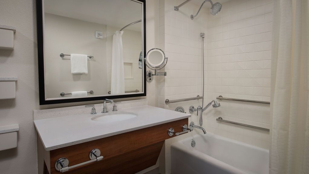 Clean white bathroom featuring a mirror, vanity counter, and bathtub with safety rails.