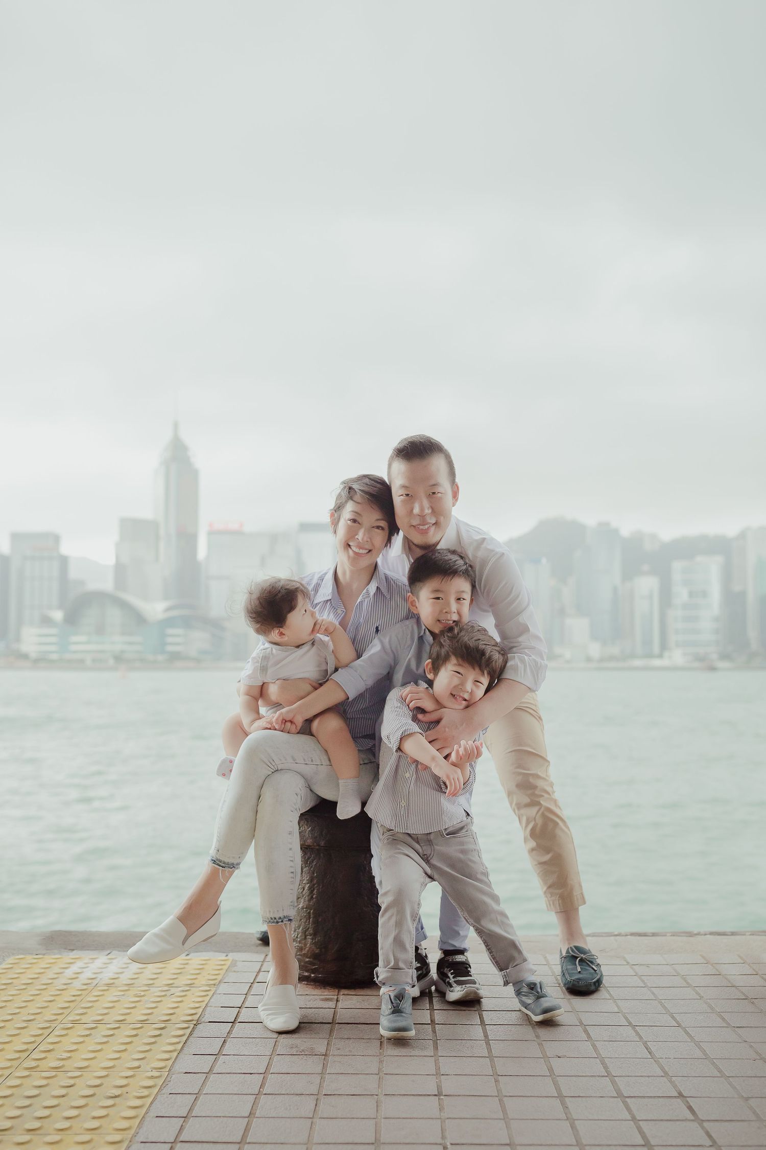 Family portrait taken at Victoria Harbour in Hong Kong with cityscape backdrop on a misty day.