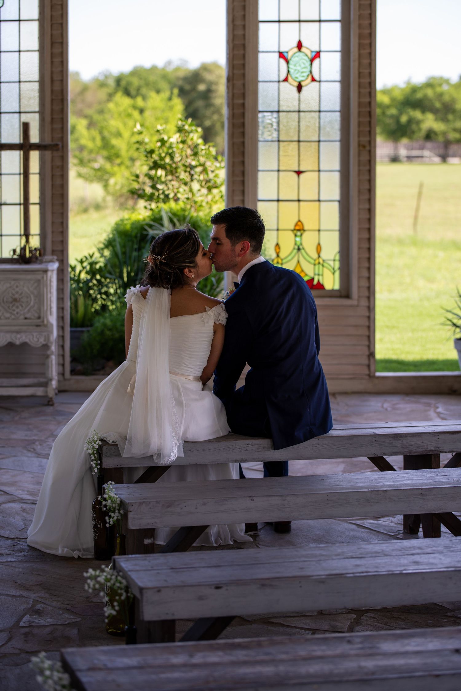 Wedding couple sharing intimate moments on wooden benches inside rustic chapel.