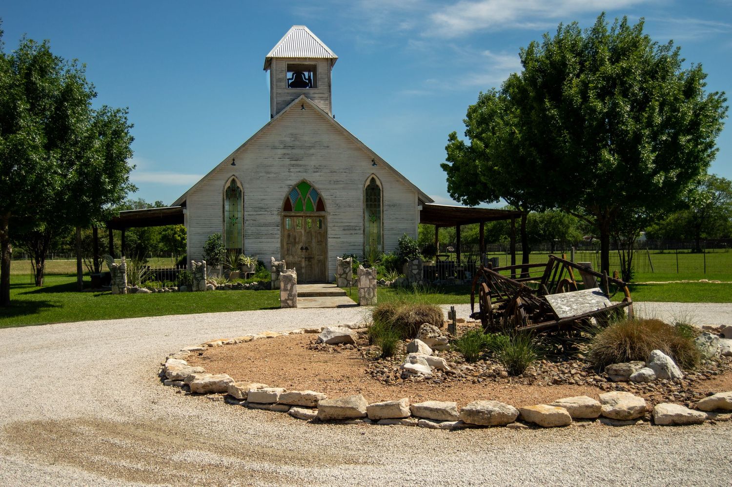 Panoramic view of a white country church with gravel path and green lawn.