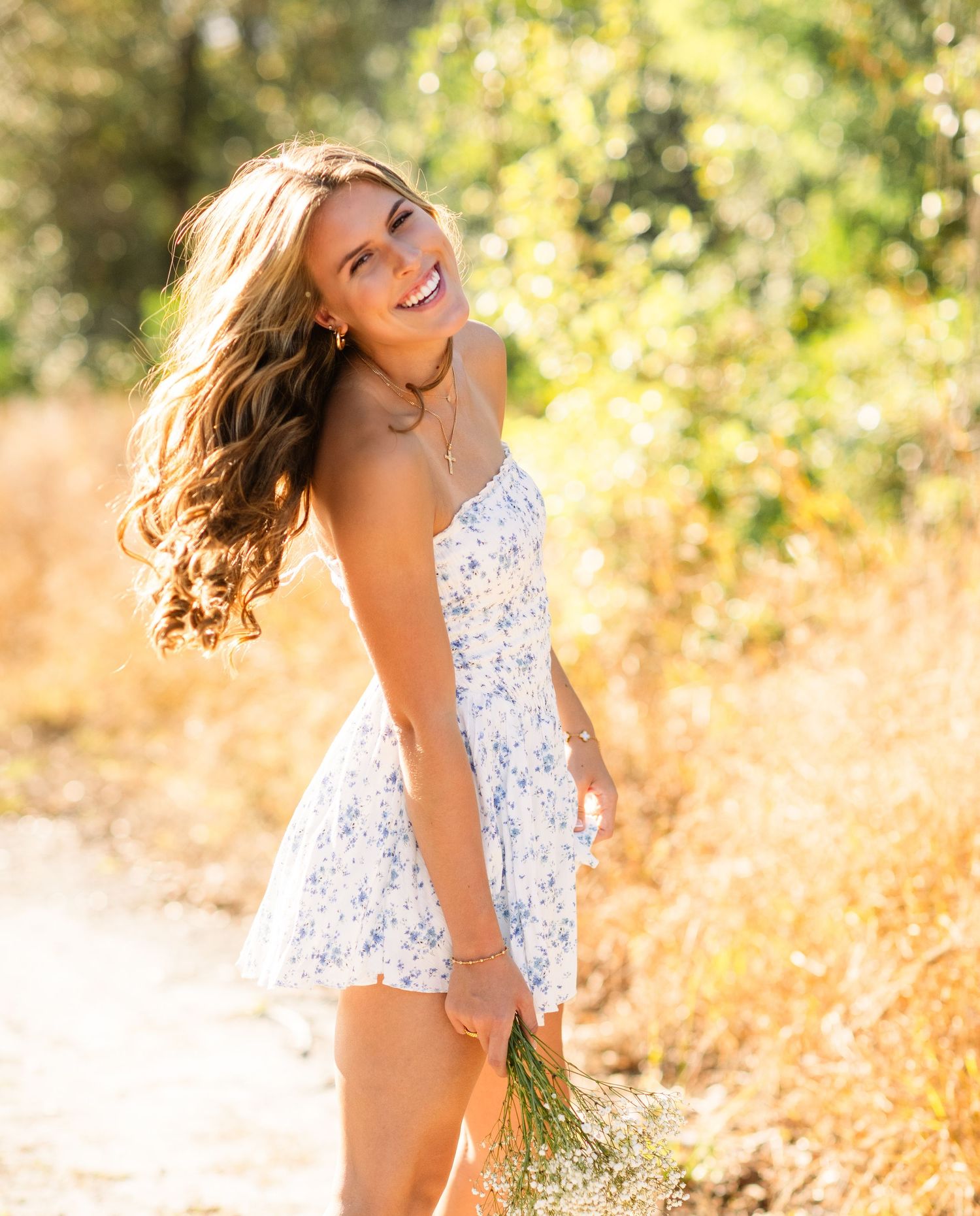 Woman in white lace dress smiles joyfully while posing in golden field during sunset.