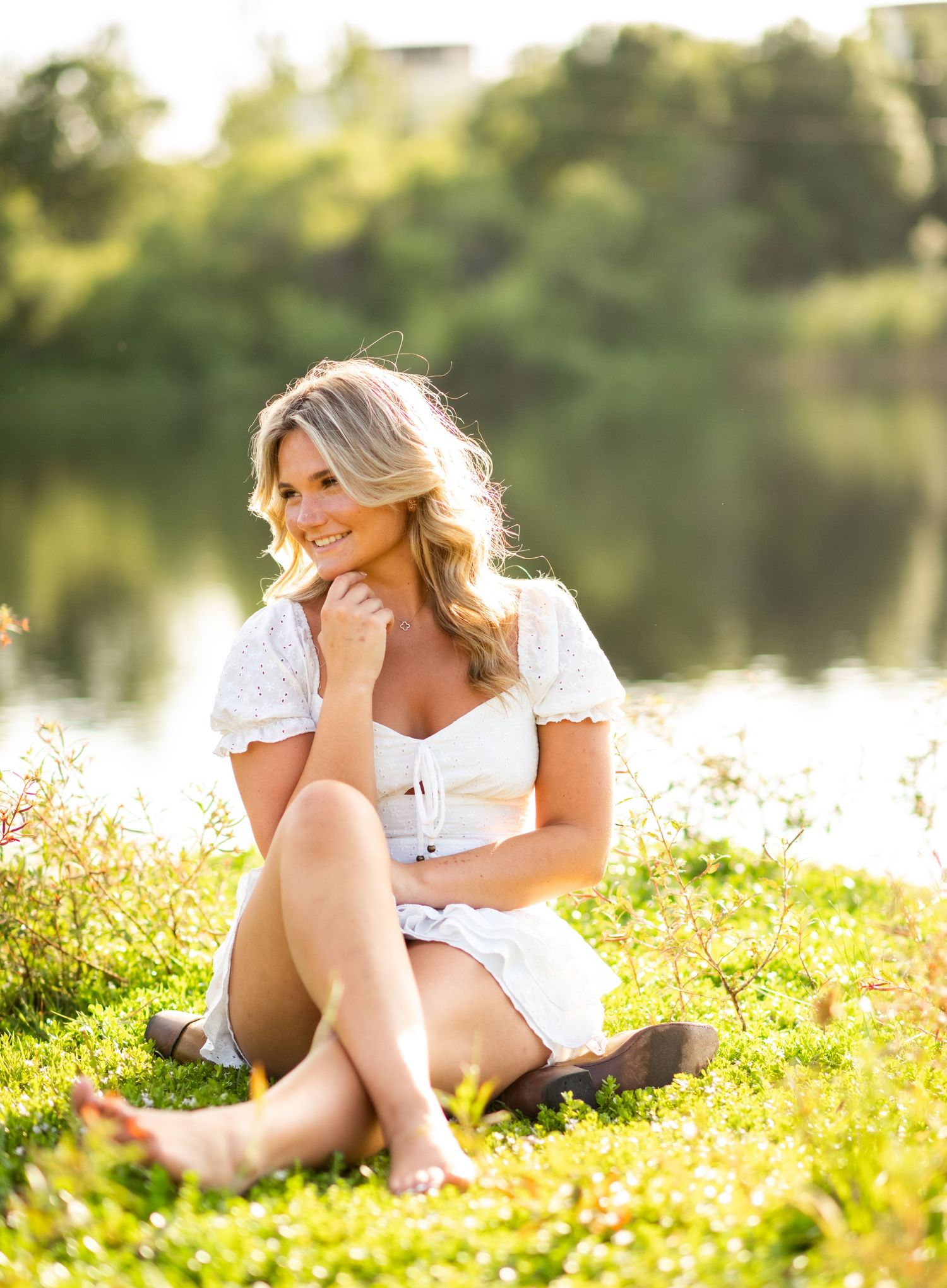 Woman in white dress reclines on sunny meadow with wildflowers during golden hour outdoor photoshoot.