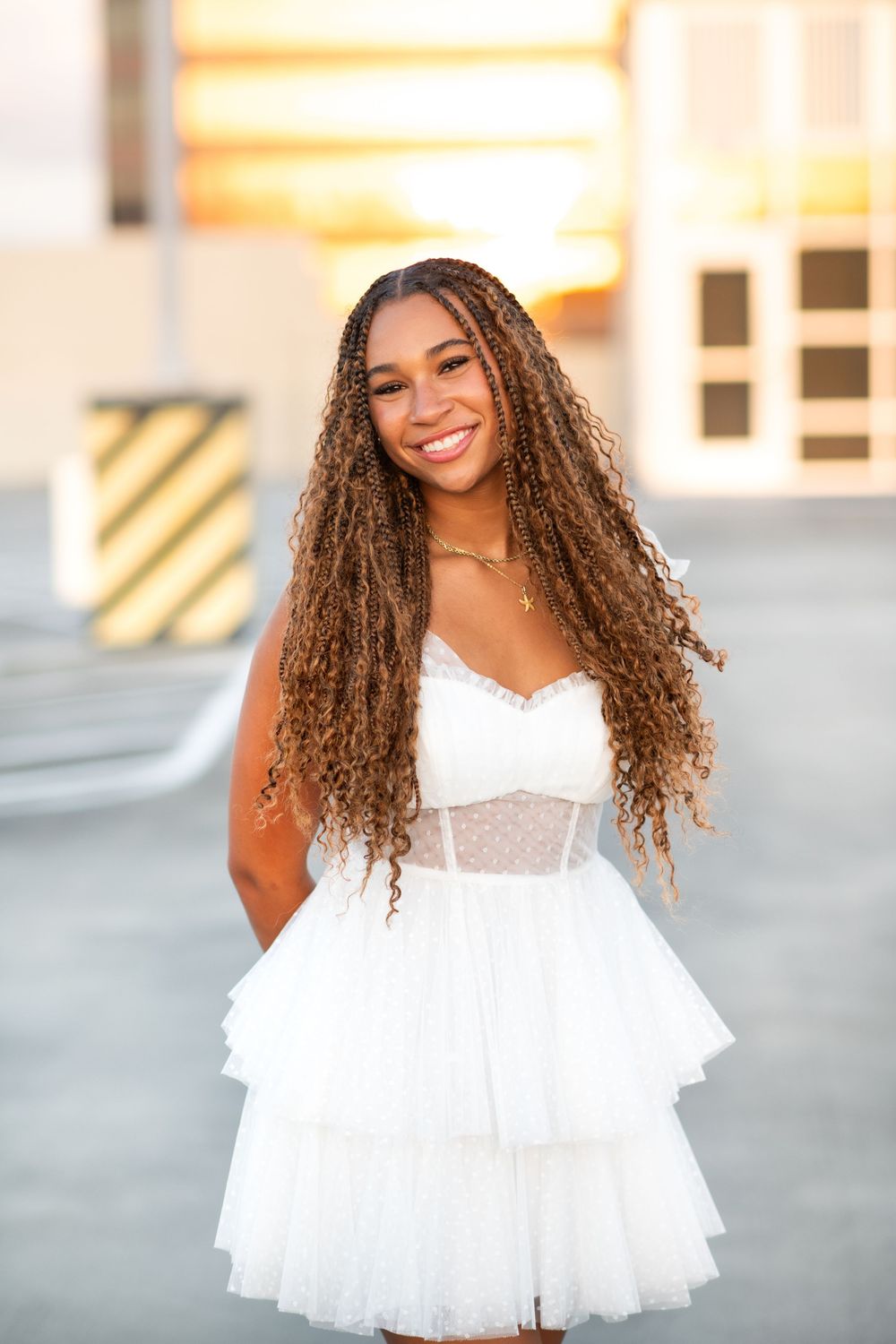 A person in a white ruffle mini dress poses with curly hair and a bright smile in an outdoor photoshoot series.