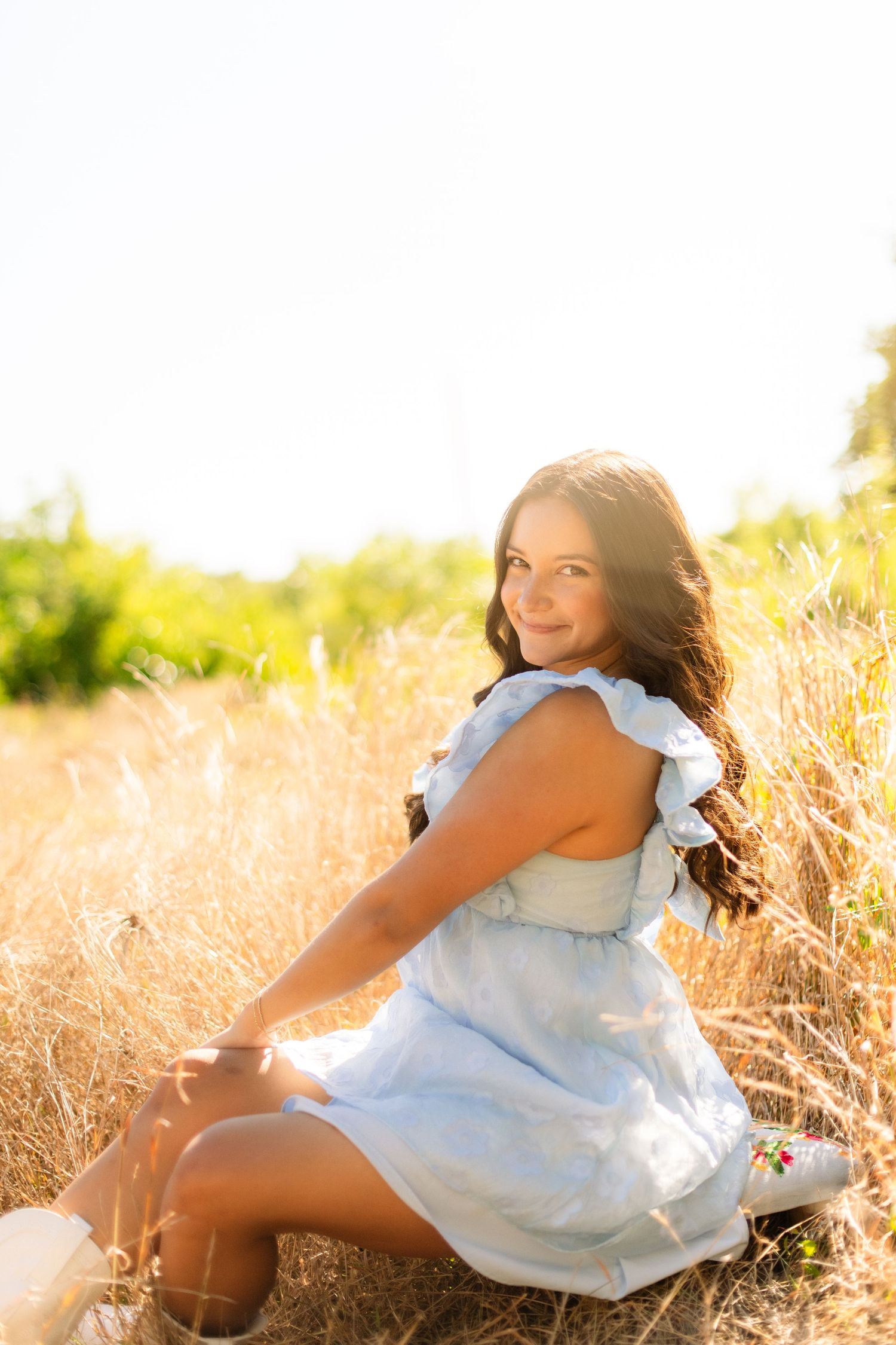 A figure in a white dress reclines in tall golden grass during sunset, creating a dreamy outdoor portrait scene.