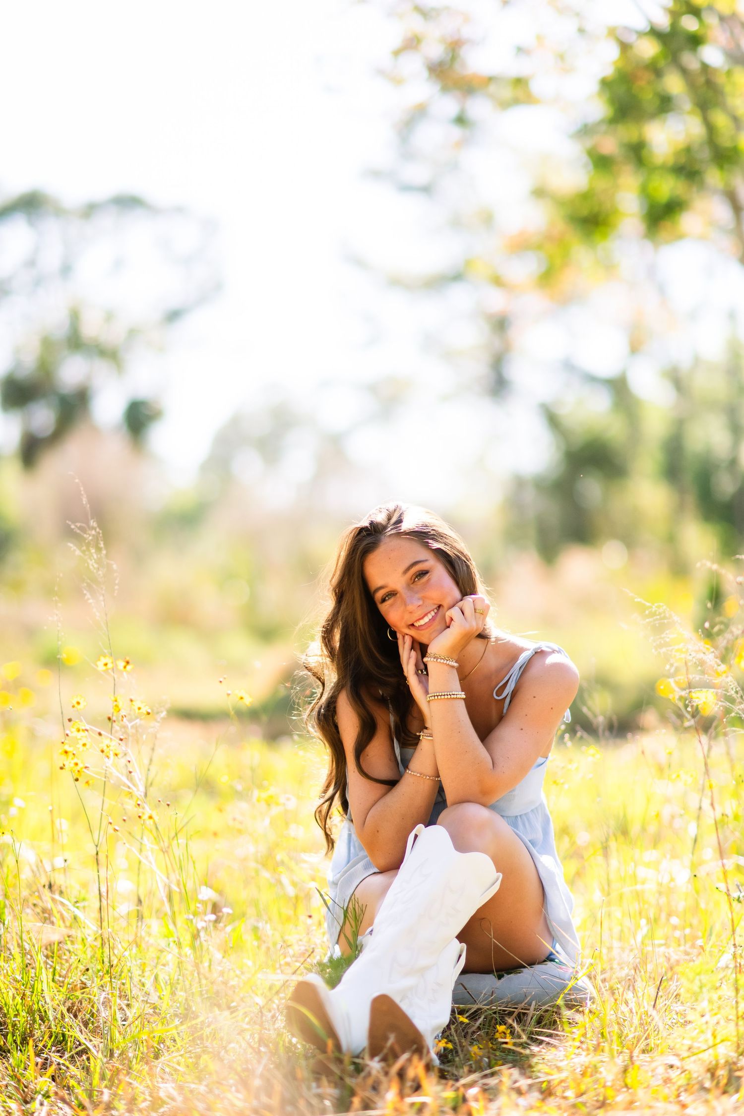 Person sitting in a sunlit meadow with tall grass and wildflowers on a bright summer day.