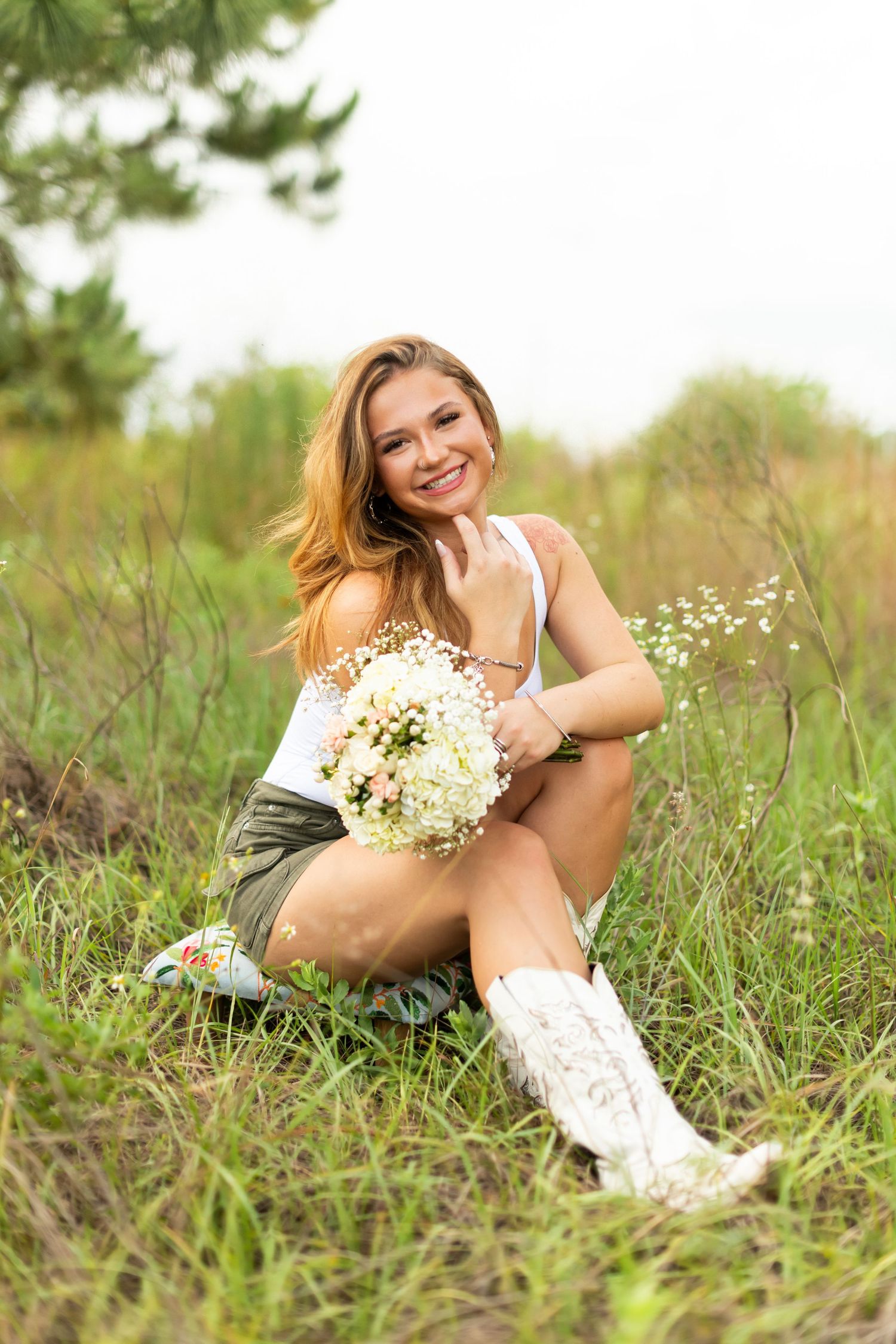A person lies in a field of grass and wildflowers wearing a white dress while holding a bouquet of baby's breath flowers.
