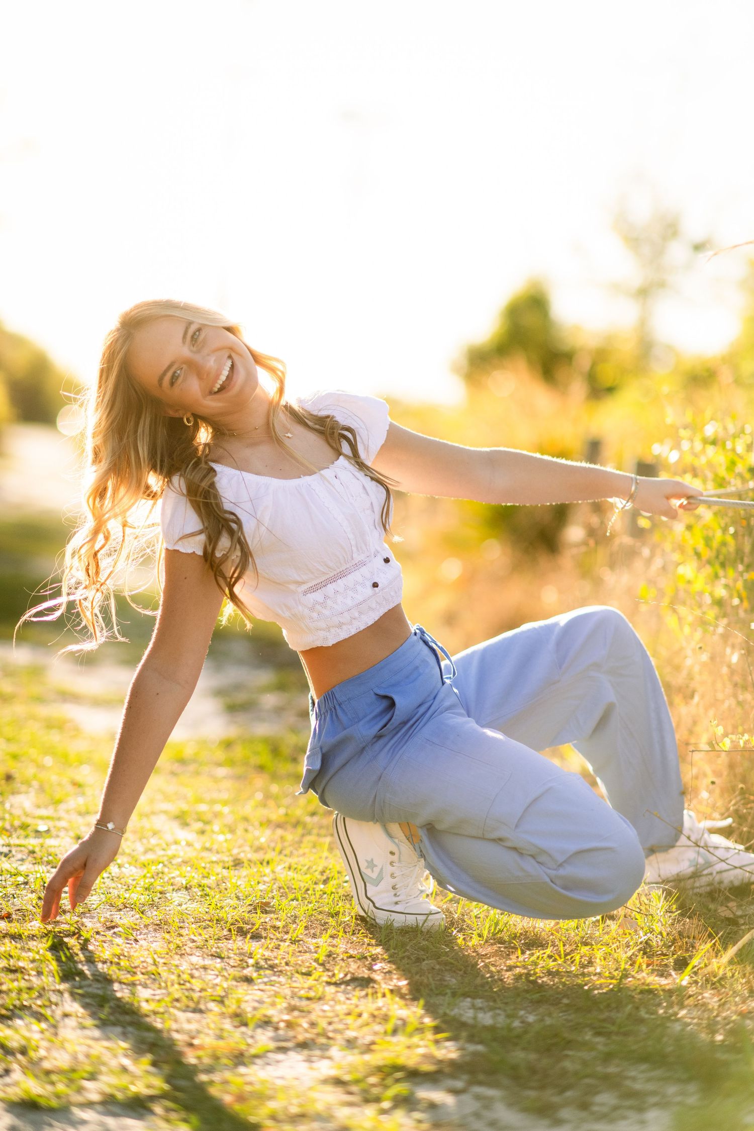 Joyful figure in white top and blue pants lying on grassy field during golden sunset light.