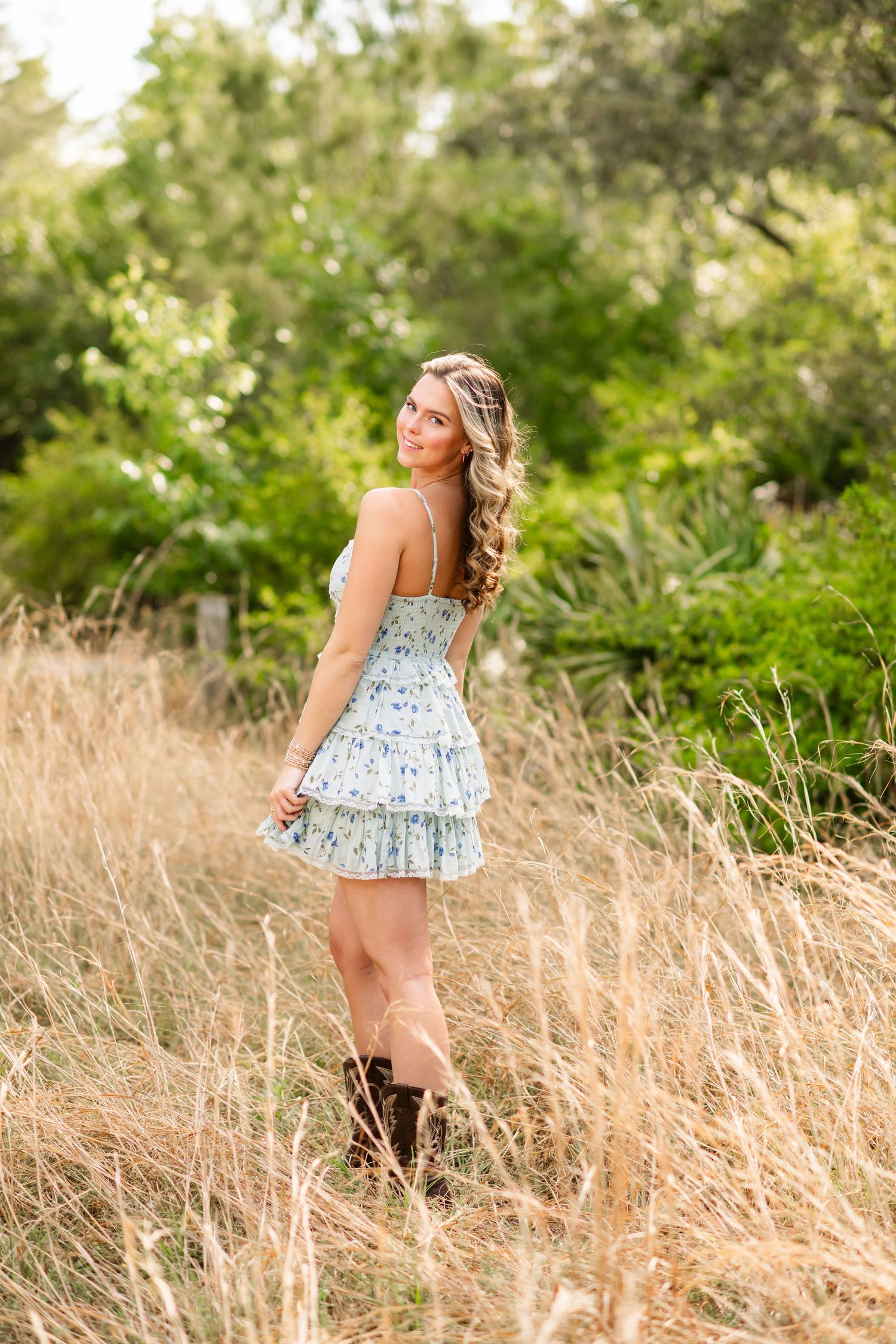 Person in a floral sundress walks through tall golden grass in a sunlit field during summer.