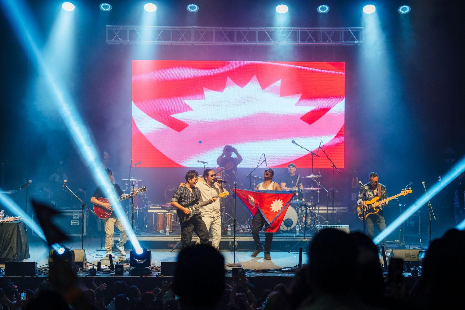 Band performs energetic concert on stage with illuminated Canadian flag backdrop and dramatic blue lighting effects.