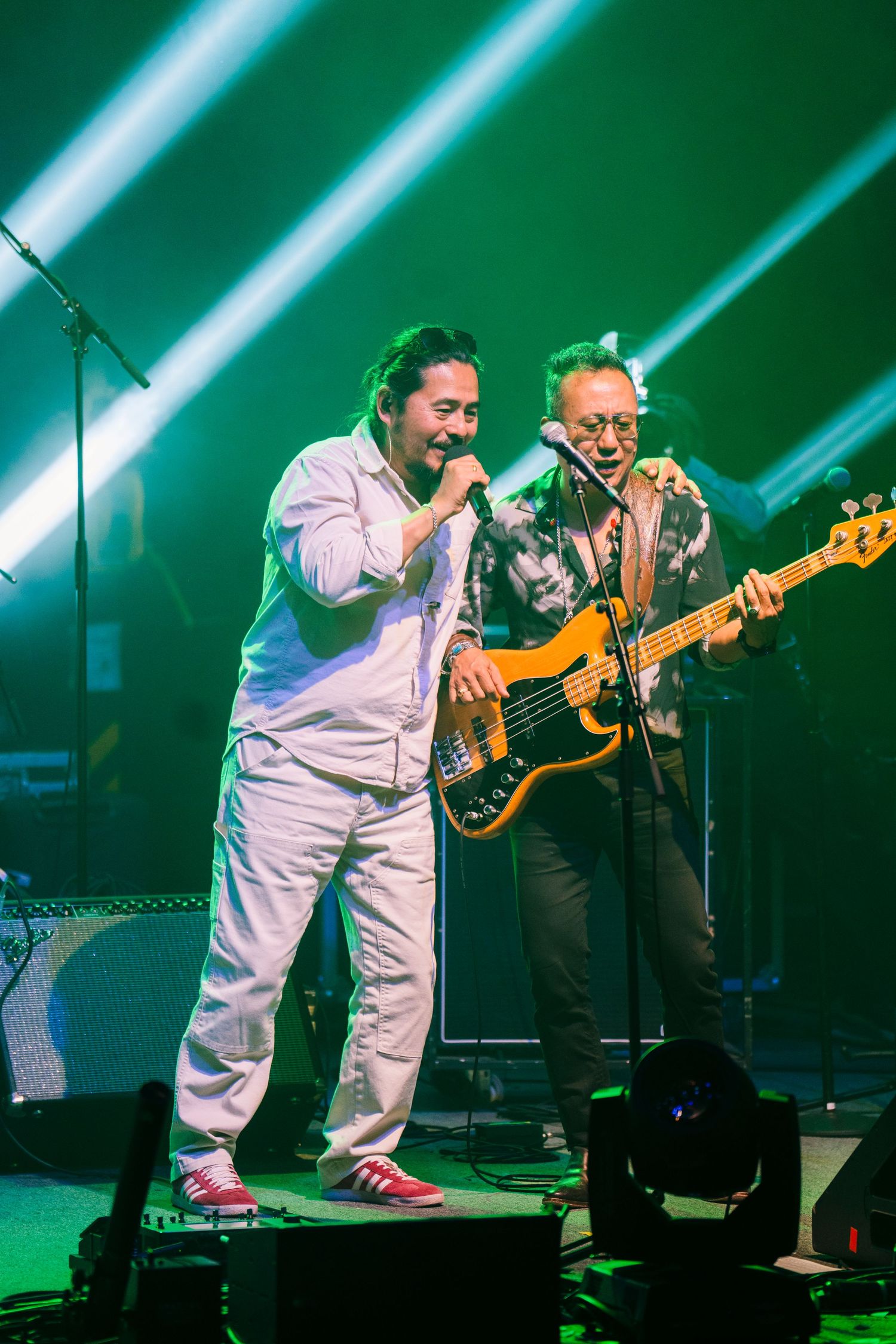 Musicians perform on stage with dramatic green lighting effects as singer and bass player entertain the crowd at live concert.