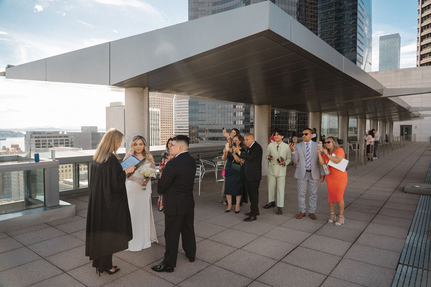 A group of people gather on a modern rooftop terrace with city buildings visible in the background.