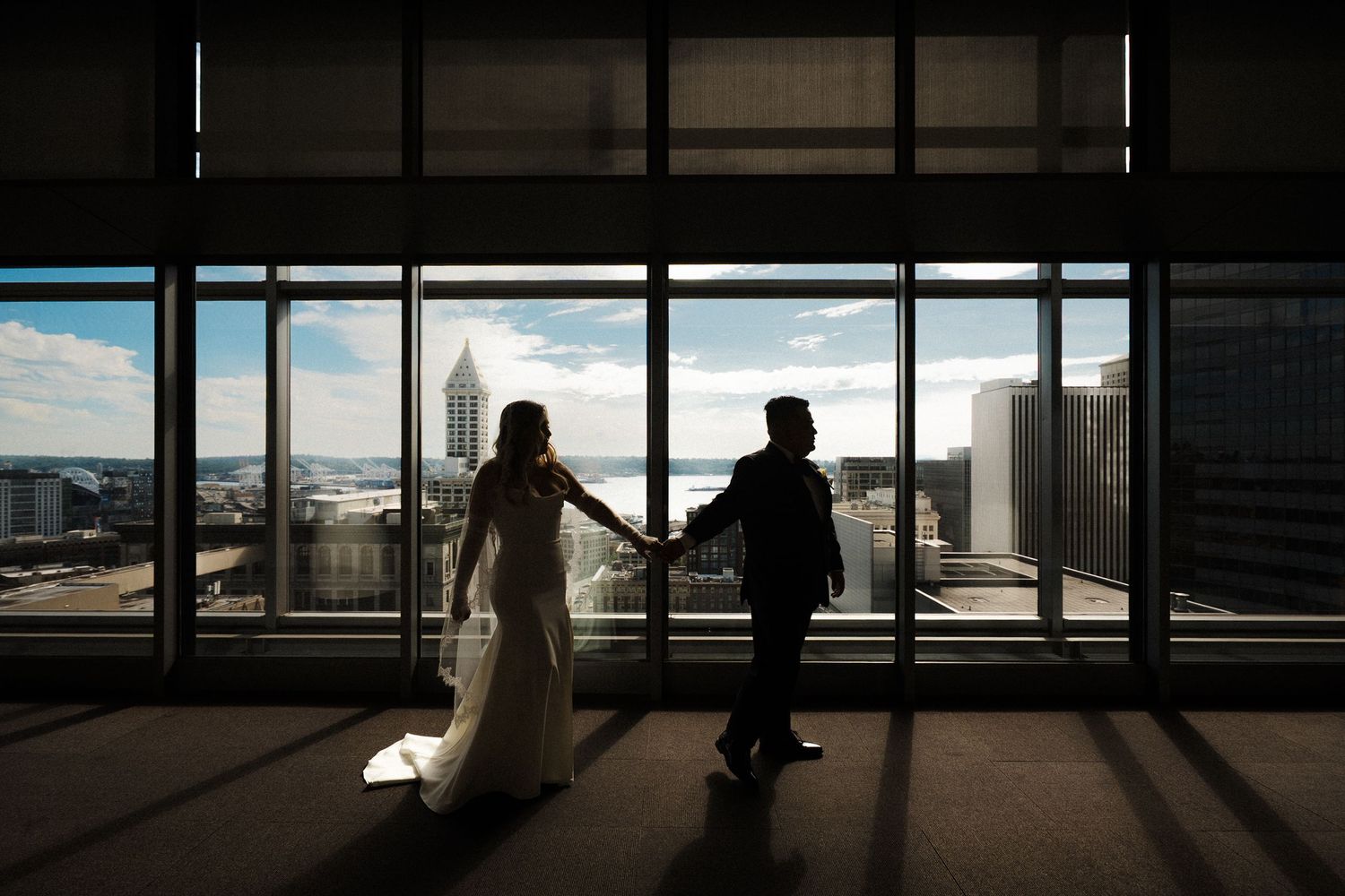 Silhouettes of people stand in contrast against large windows overlooking a city skyline at sunset.