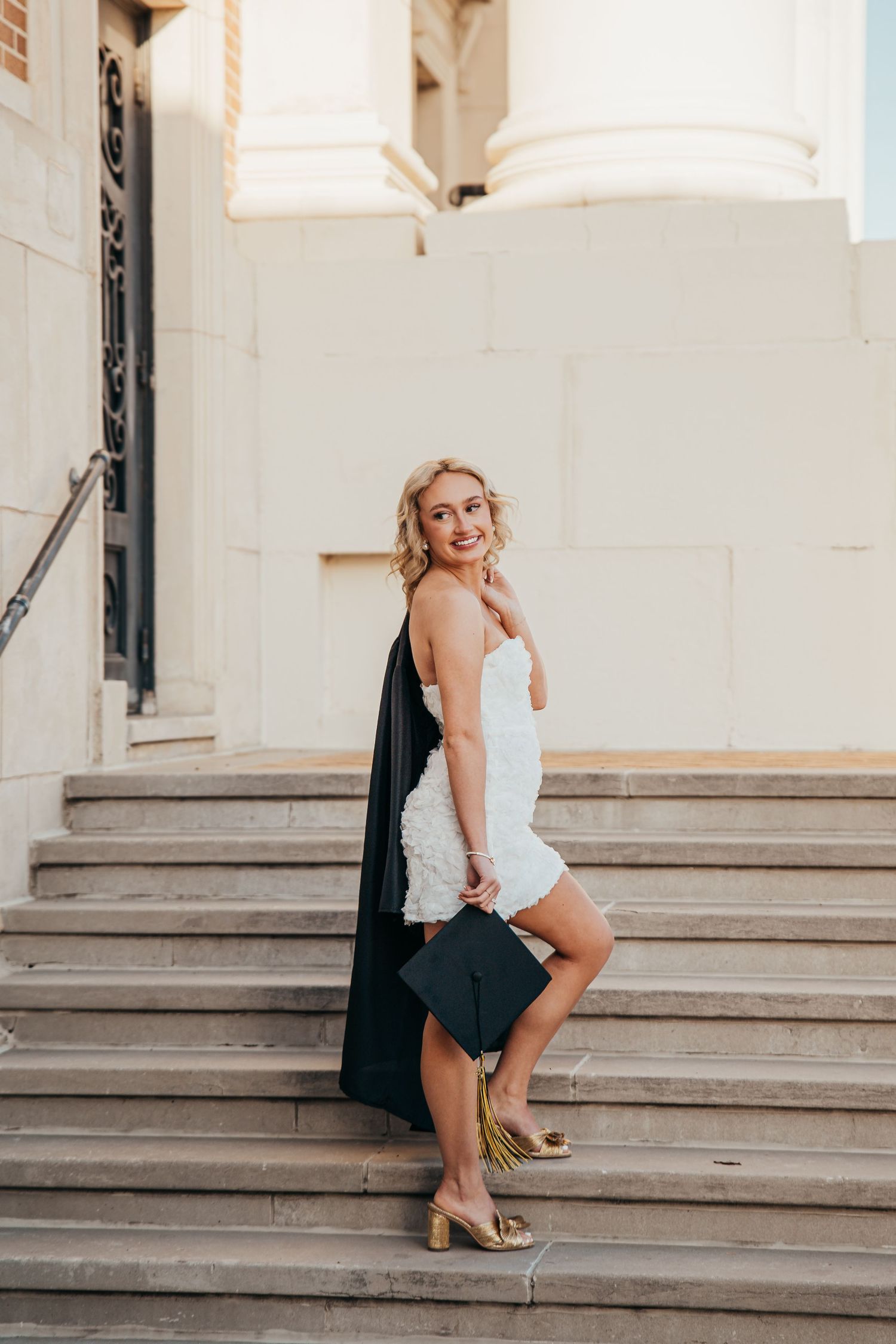 Woman in white dress poses elegantly on concrete steps in summer.