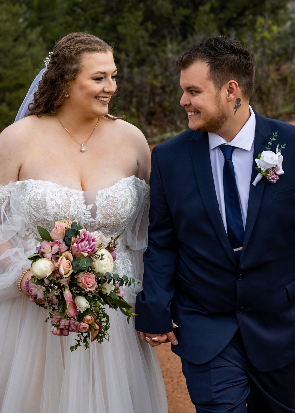 A romantic wedding couple shares a joyful moment together while holding a pink and white floral bouquet.